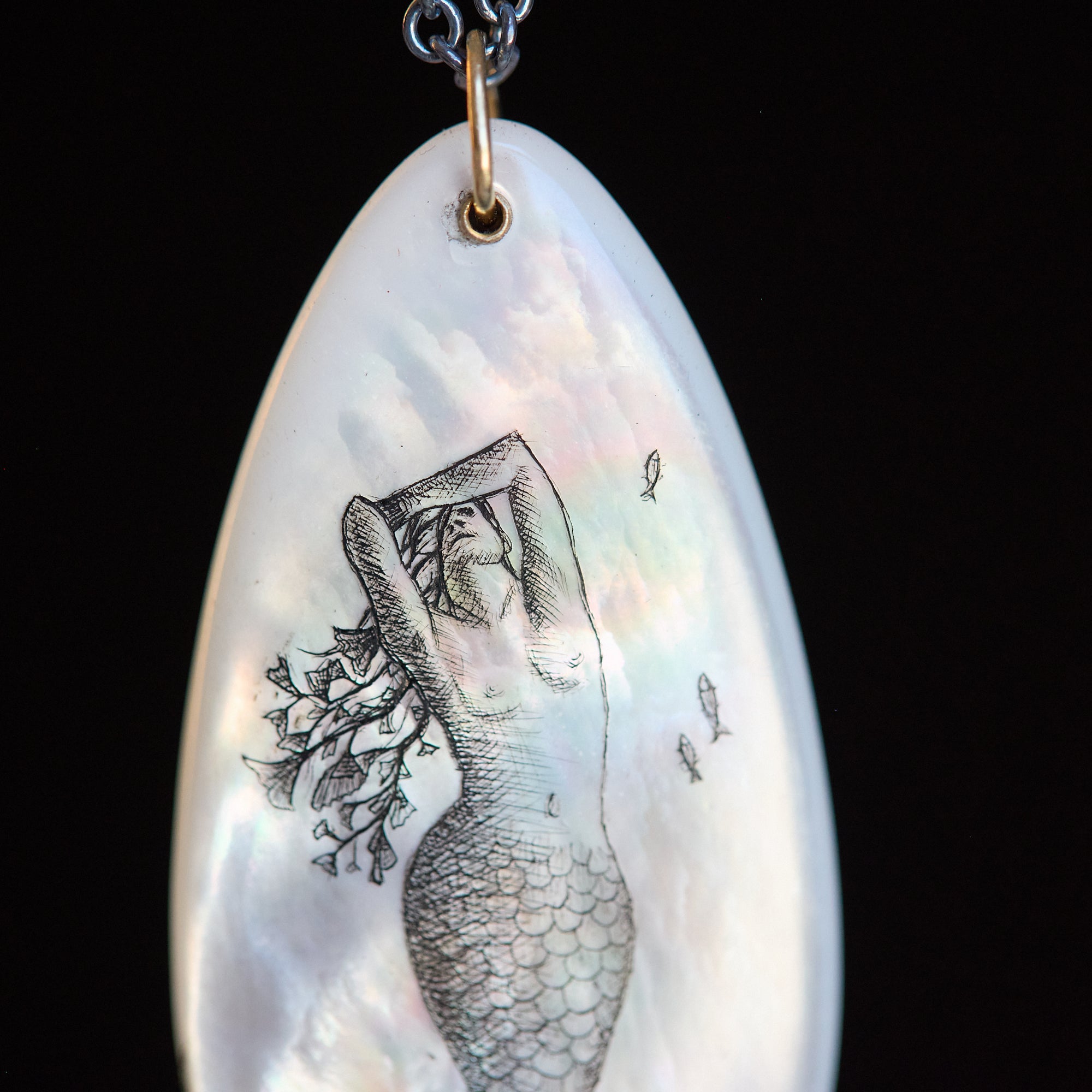 Shell pendant with mermaid illustration on a black background