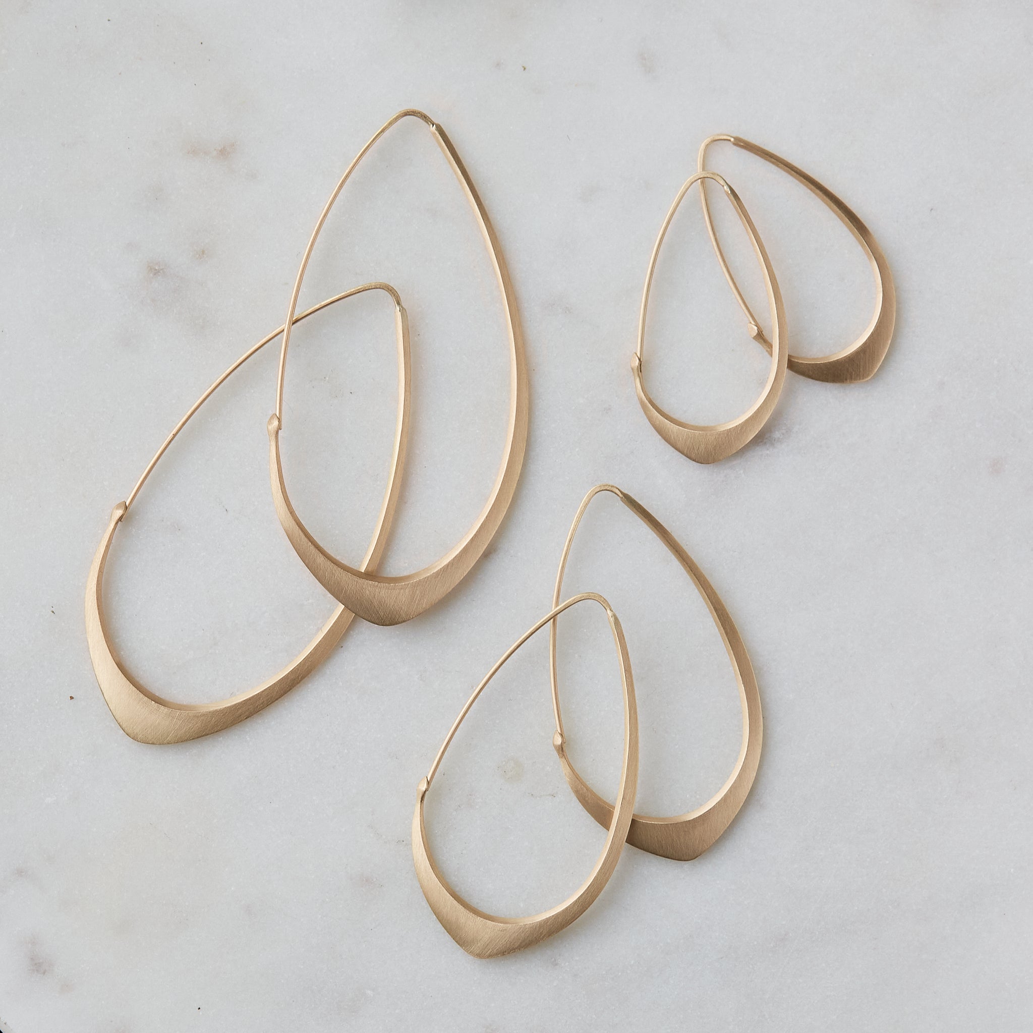 three pairs of facet hoops laid out on marble, in three different sizes, in gold