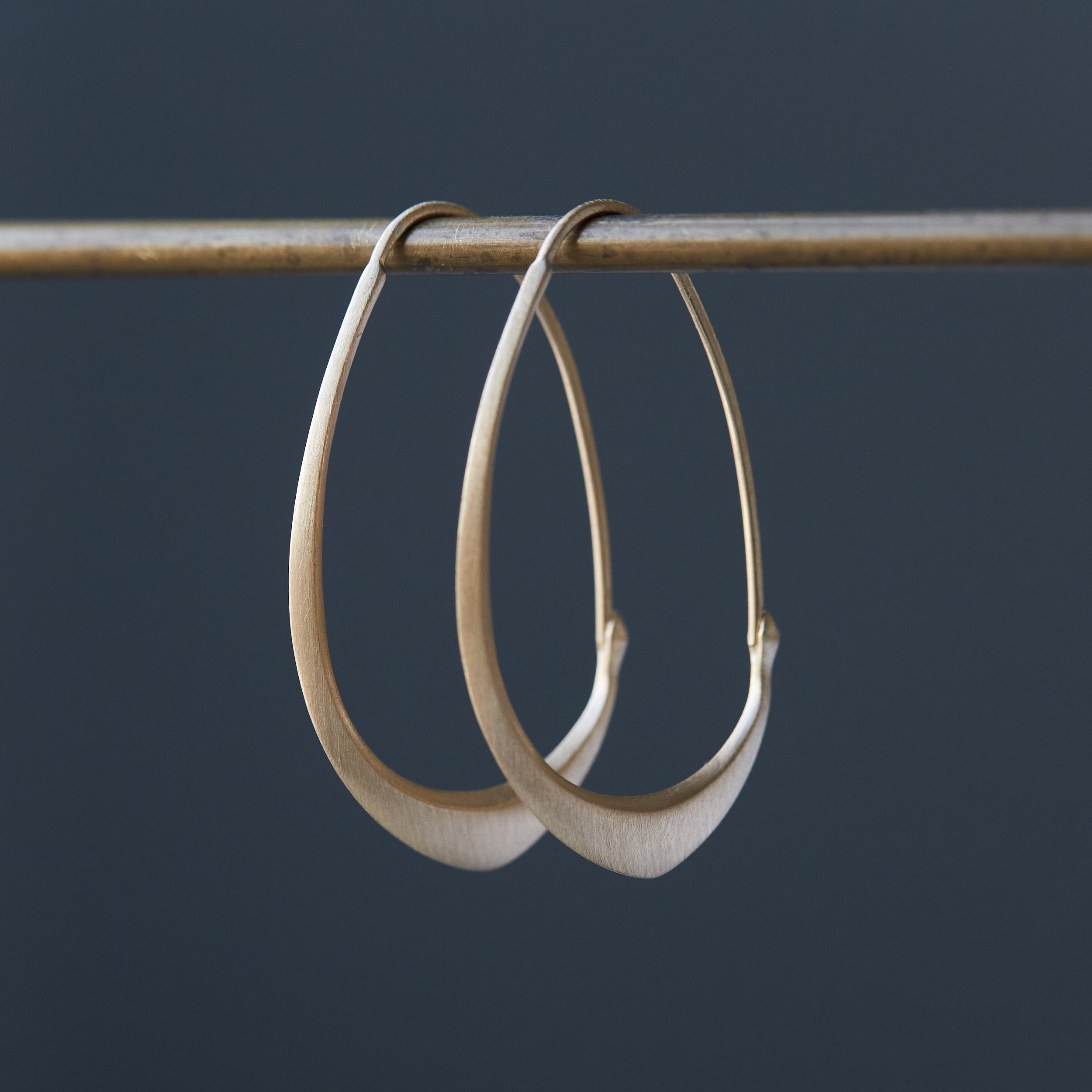 small gold facet hoops hanging from a bar against a grey background