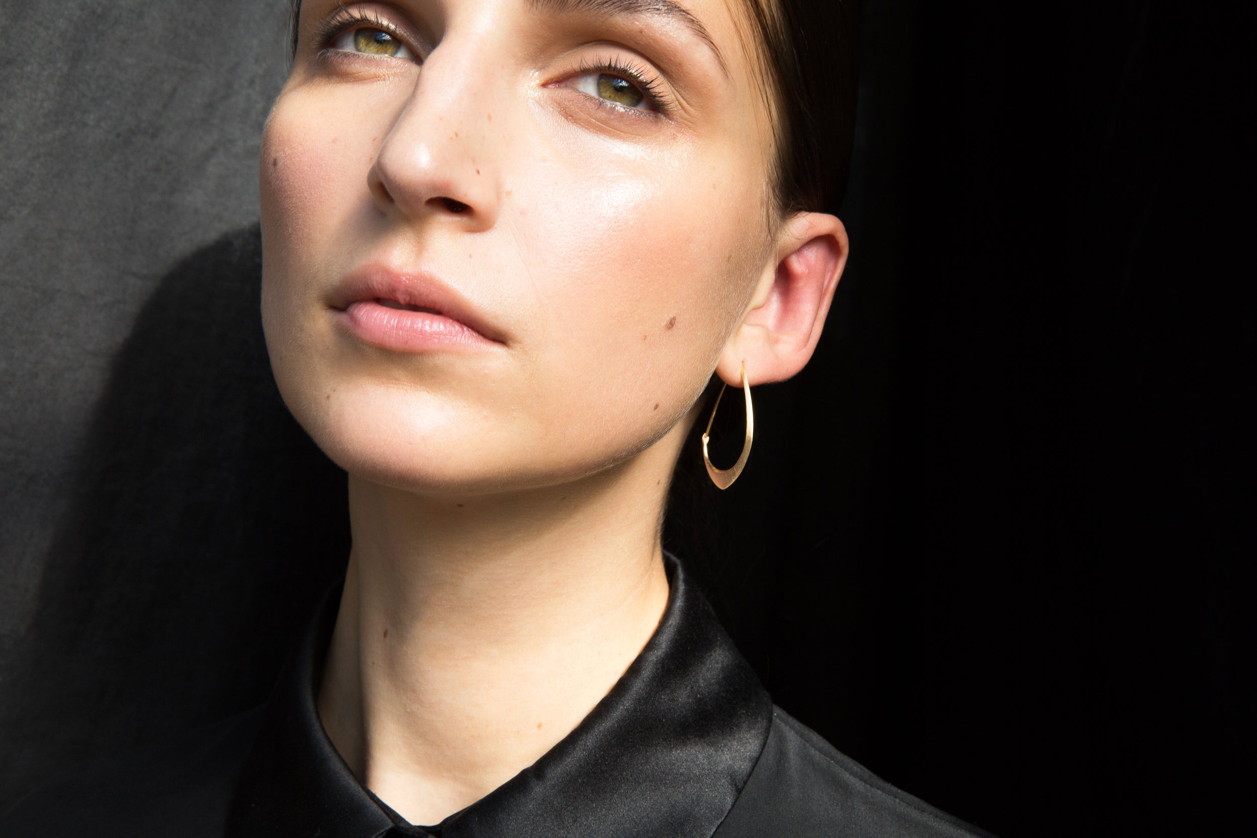small gold facet hoops shown on person against black