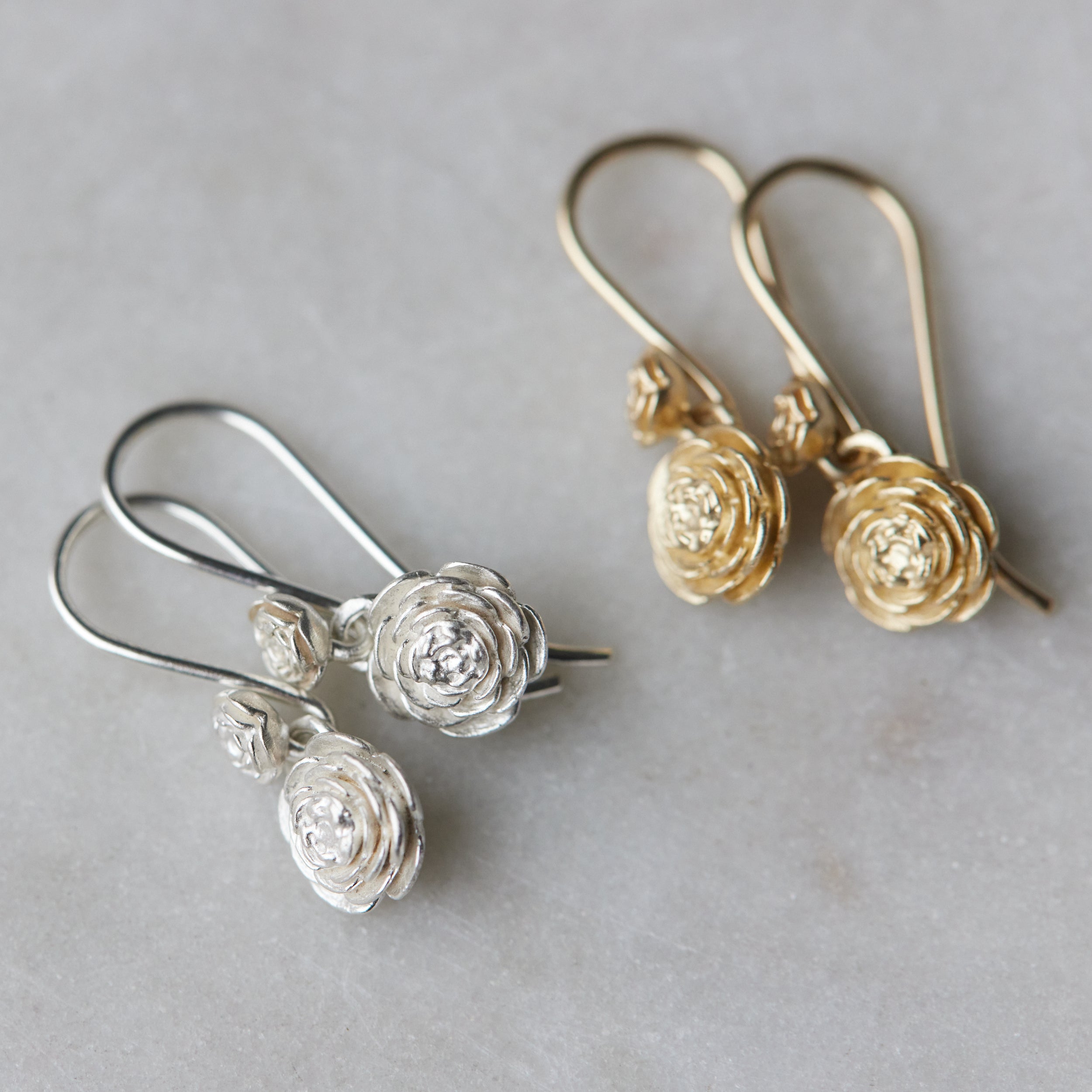 two pairs of double rose garden earrings. The pair on the left is silver, the pair on the right is gold.
