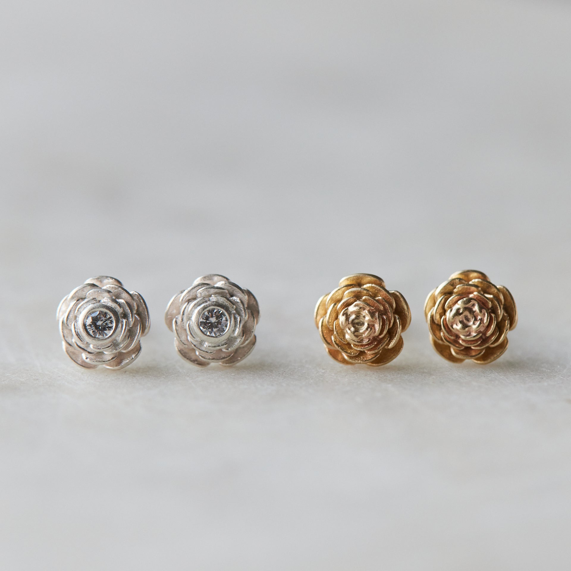 two pairs of rose garden studs- the left pair is silver with diamonds, the right pair is yellow gold with no diamonds.
