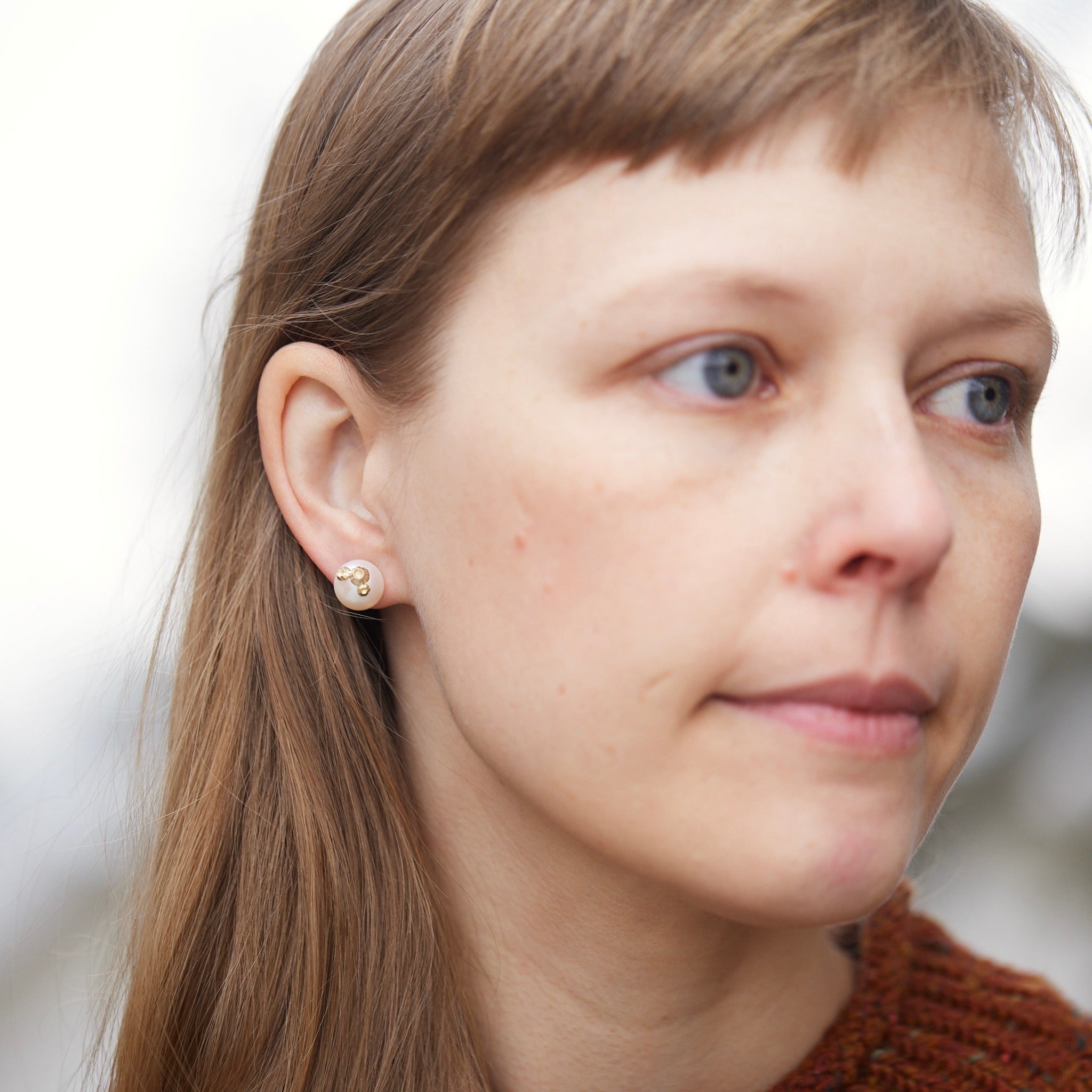 Large pearl studs with gold barnacles, photographed on person.