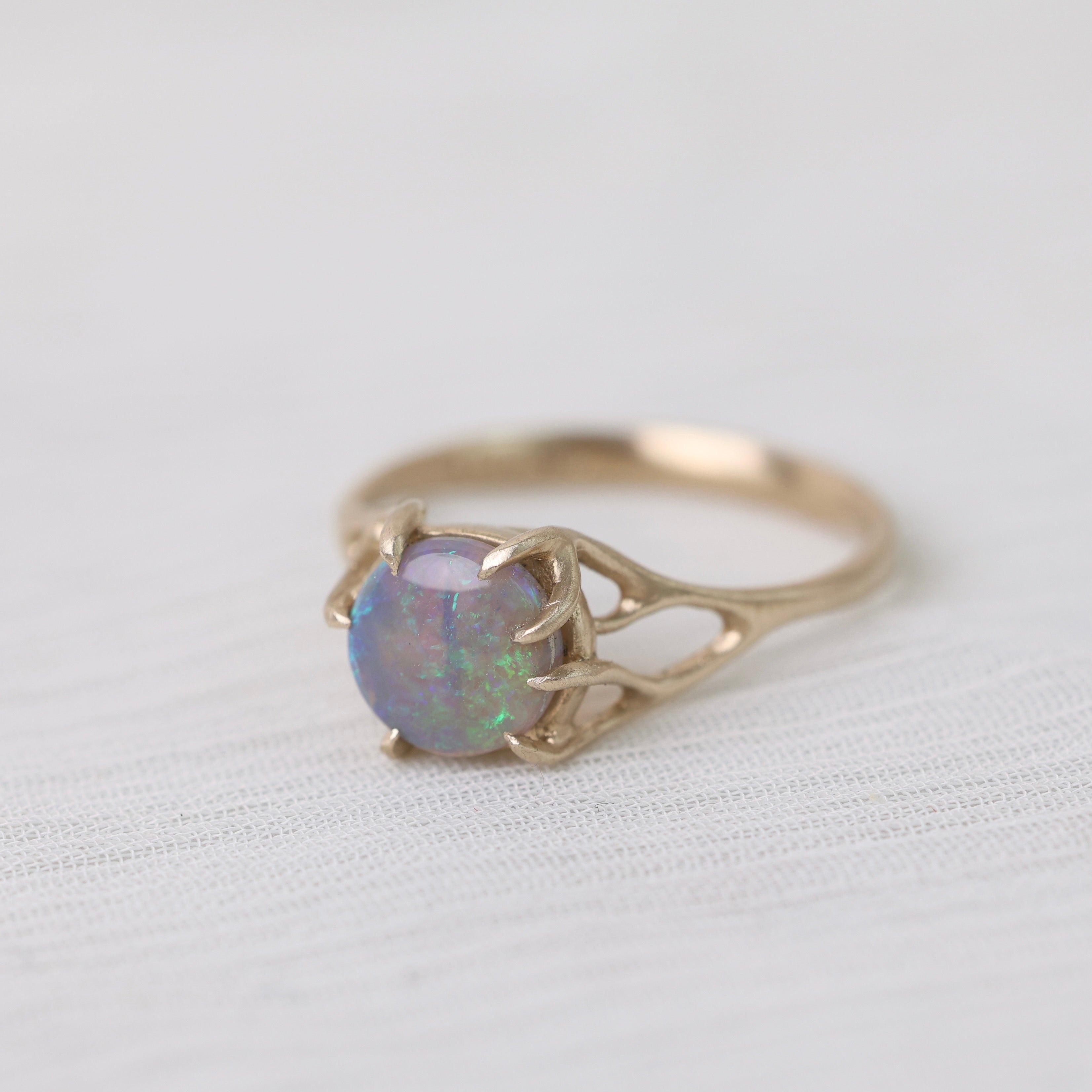 Colorful opal in delicate gold prongs on a white background