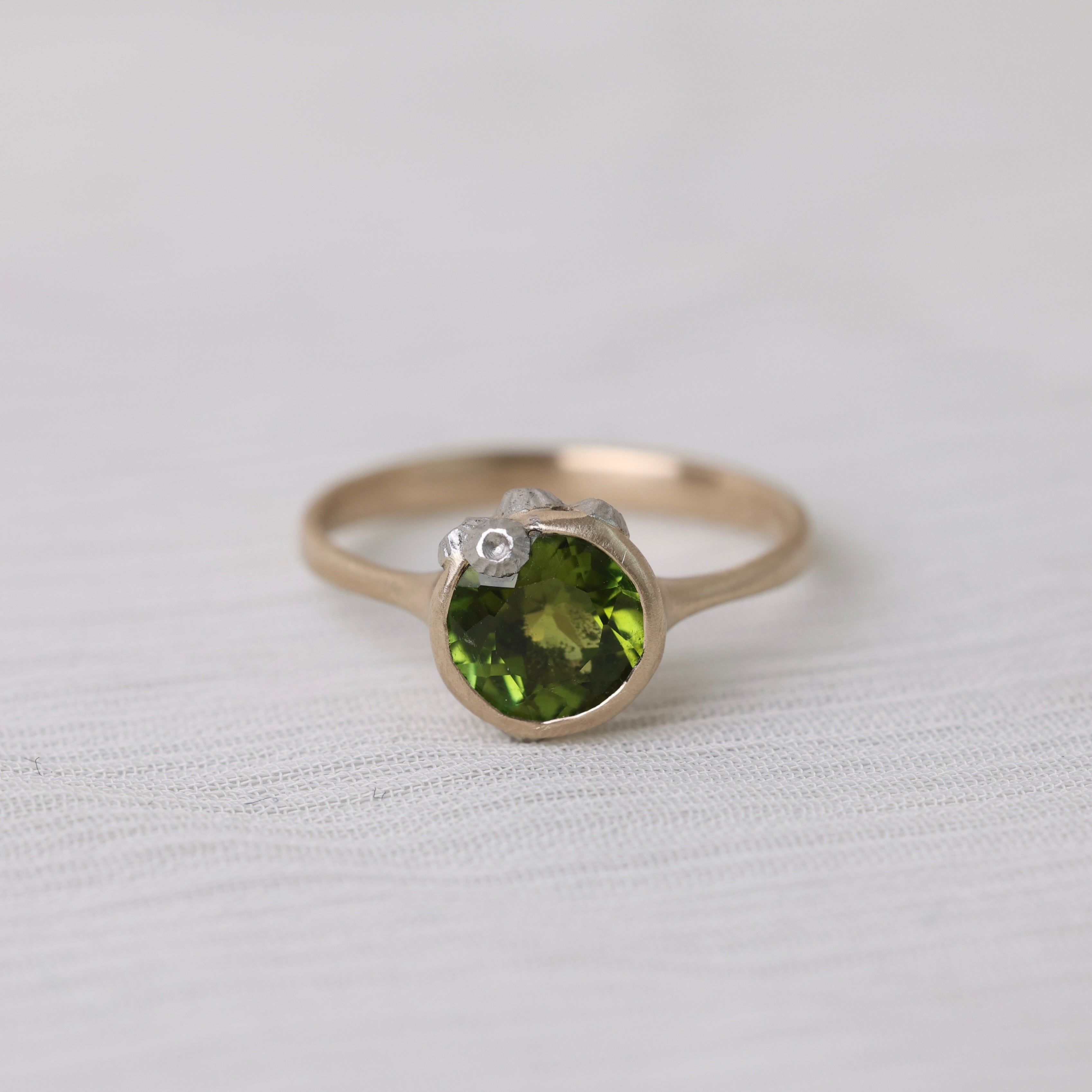 Gold ring with bright green stone and silver barnacles on white background
