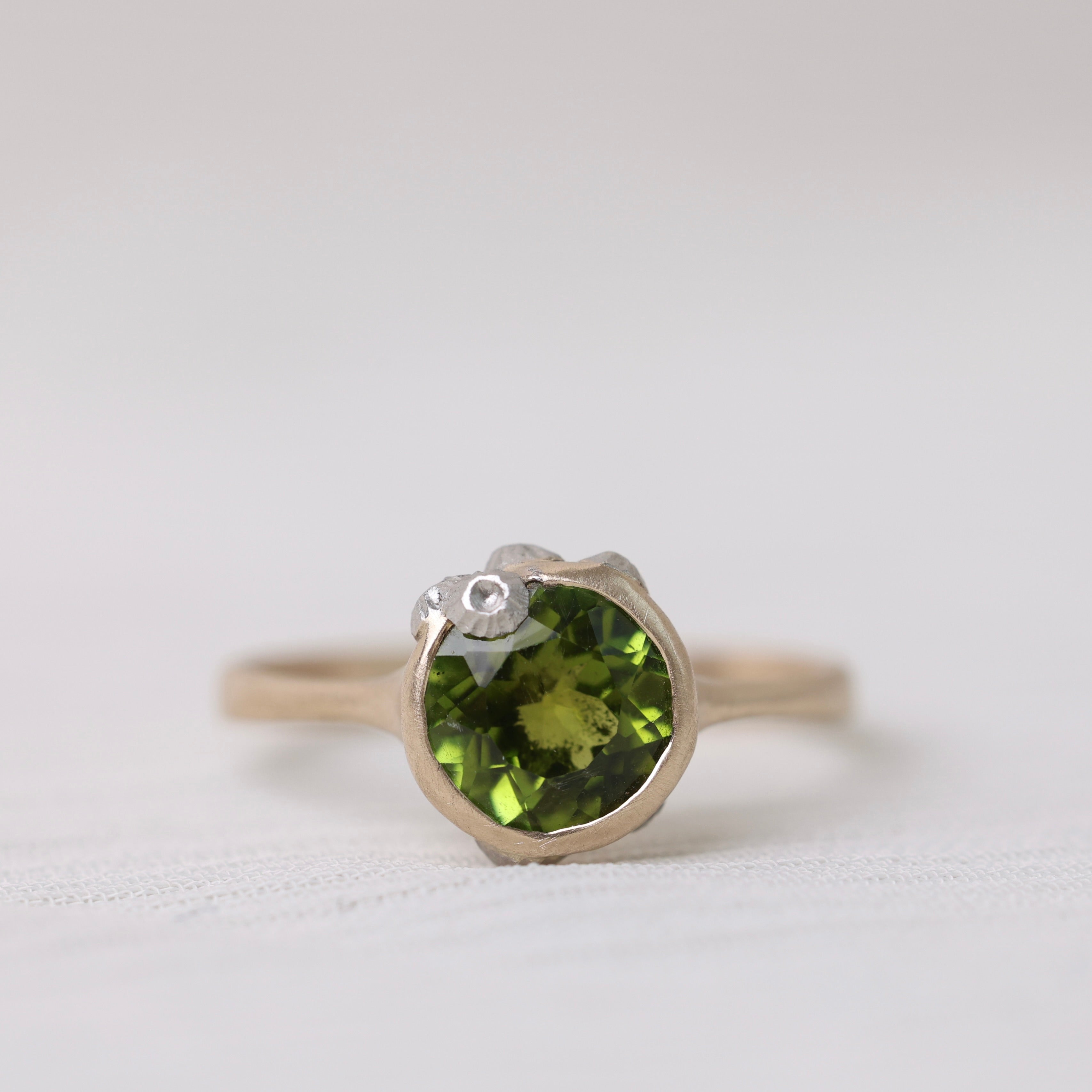 Gold ring with bright green stone and silver barnacles on white background