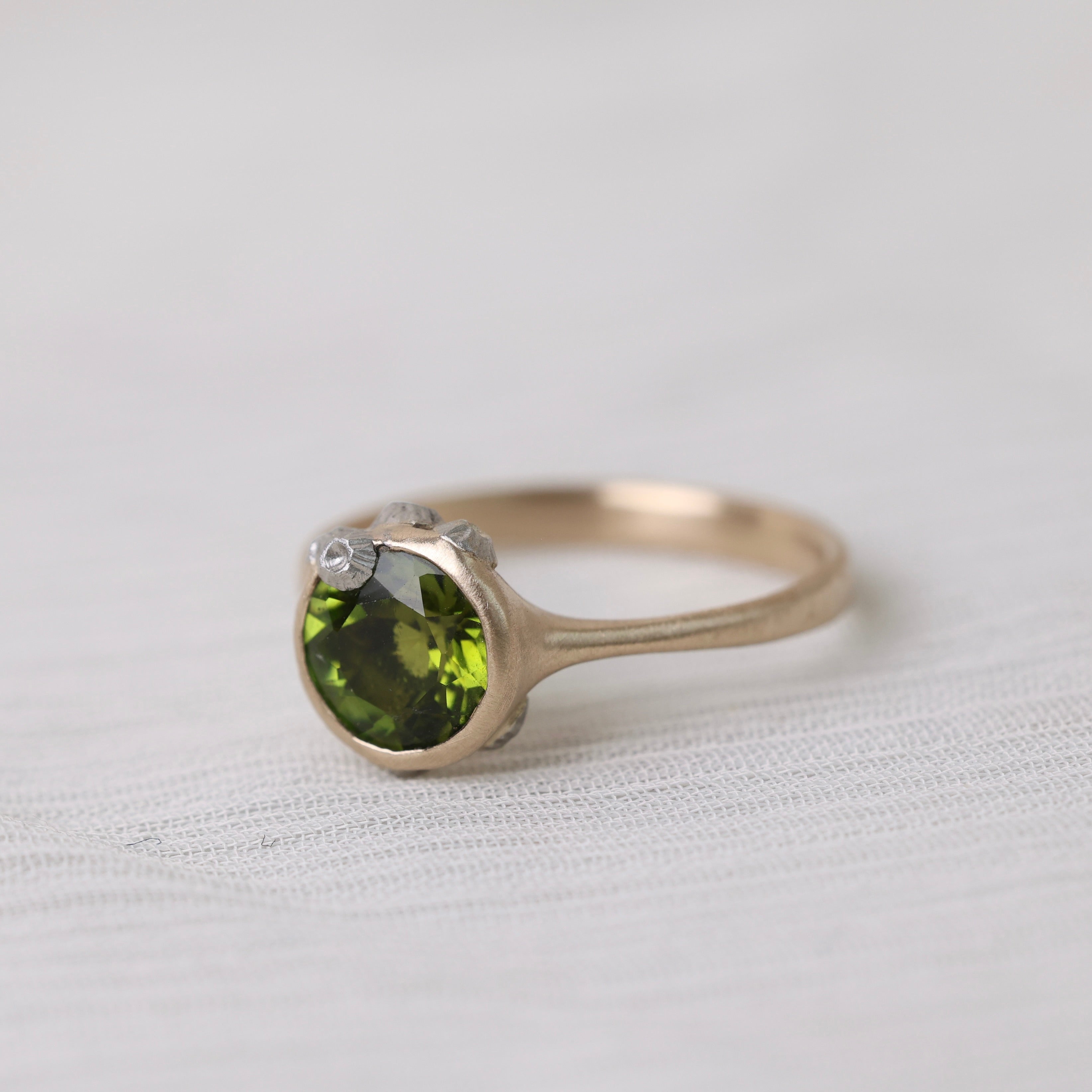 Gold ring with bright green stone and silver barnacles on white background