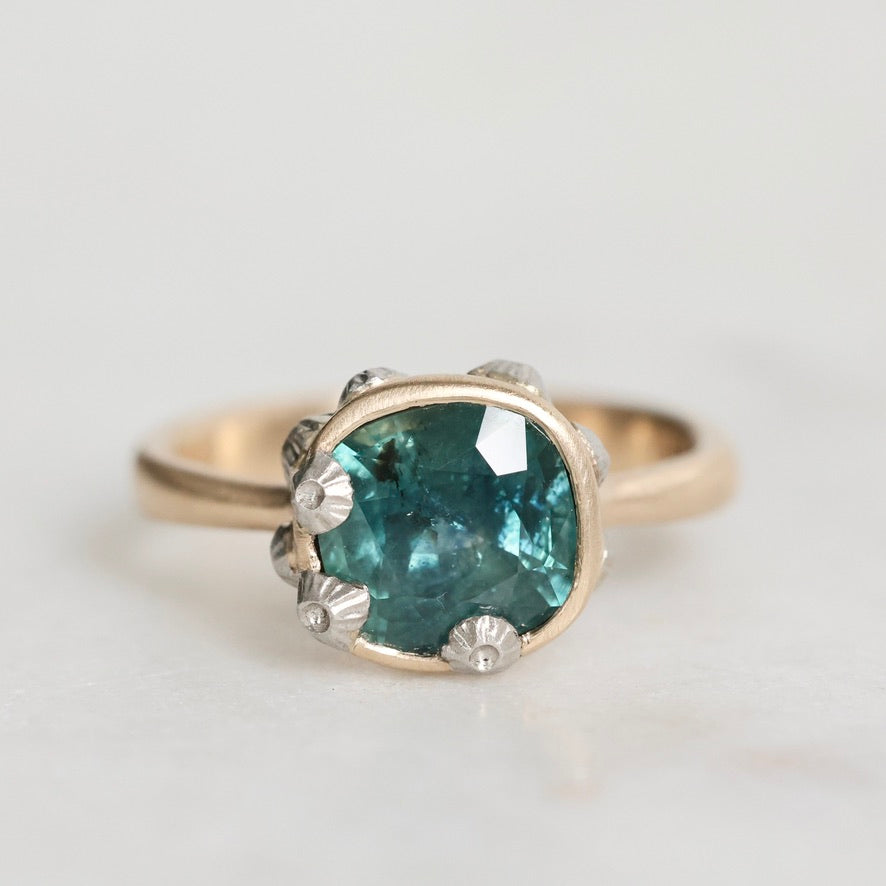 Ring with a green gemstone and gold band on a light gray background