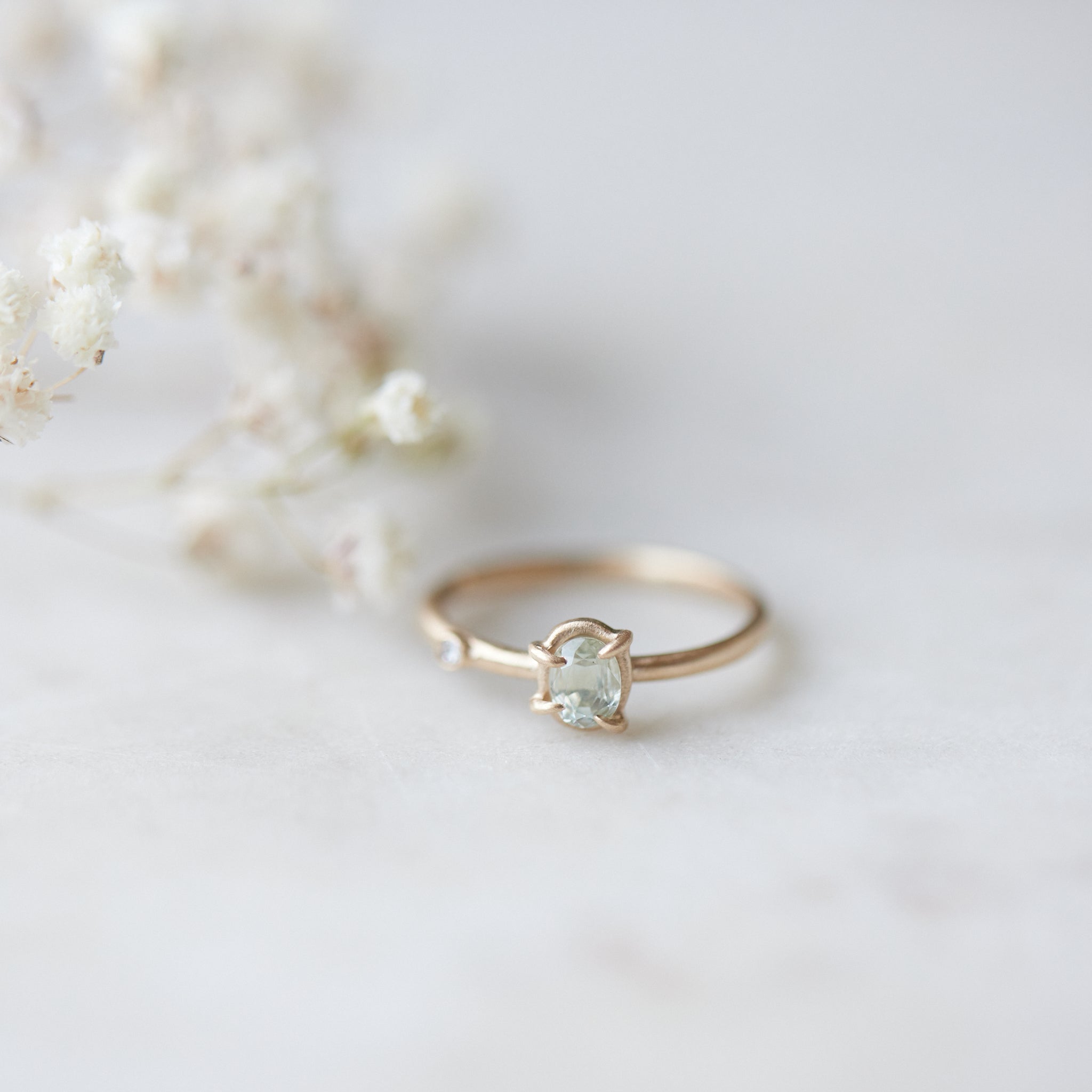 side view of milky clean montana sapphire oval set in a gold ring via a-symetrical prongs and a single diamond accent off-set on the band.