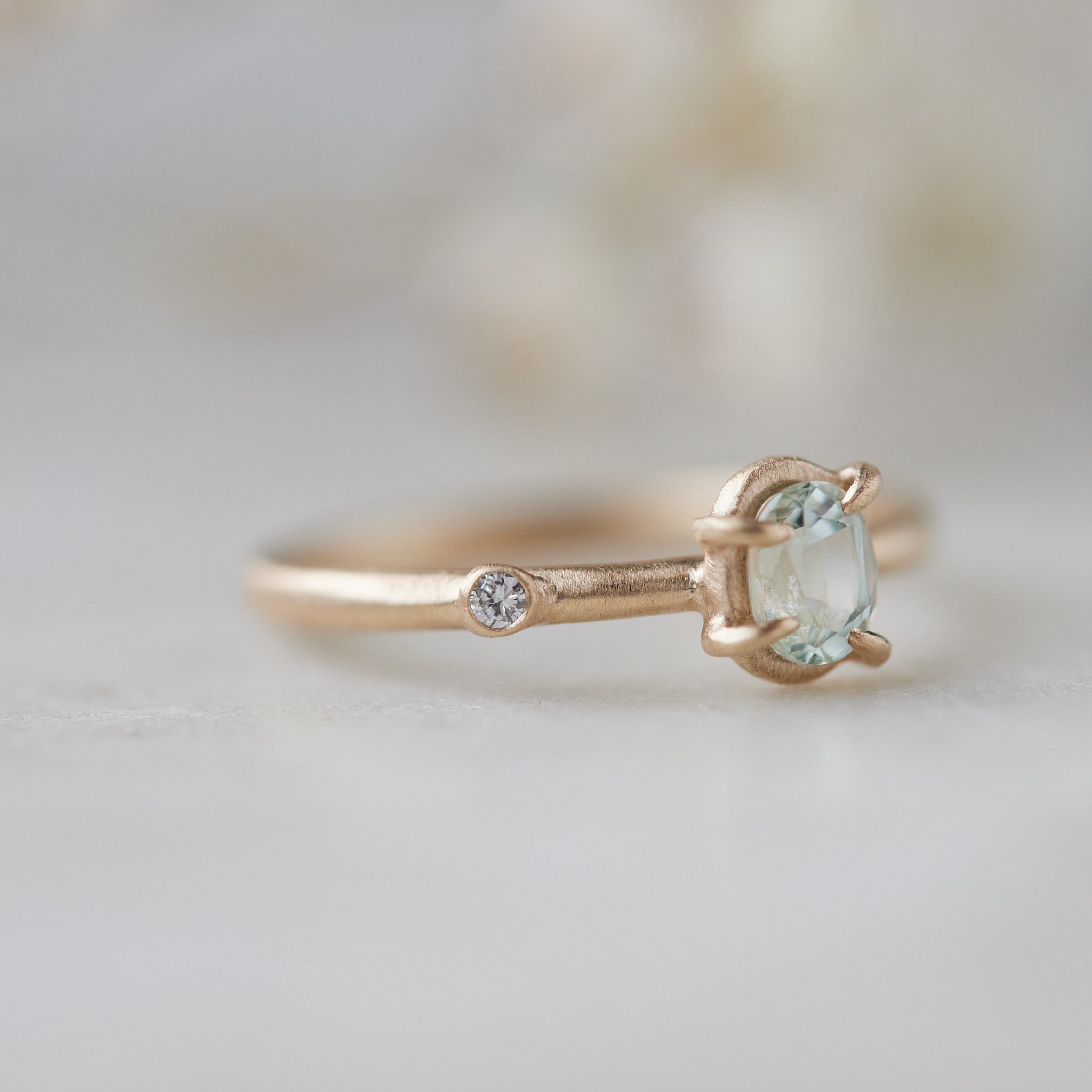 side view of milky clean montana sapphire oval set in a gold ring via a-symetrical prongs and a single diamond accent off-set on the band.