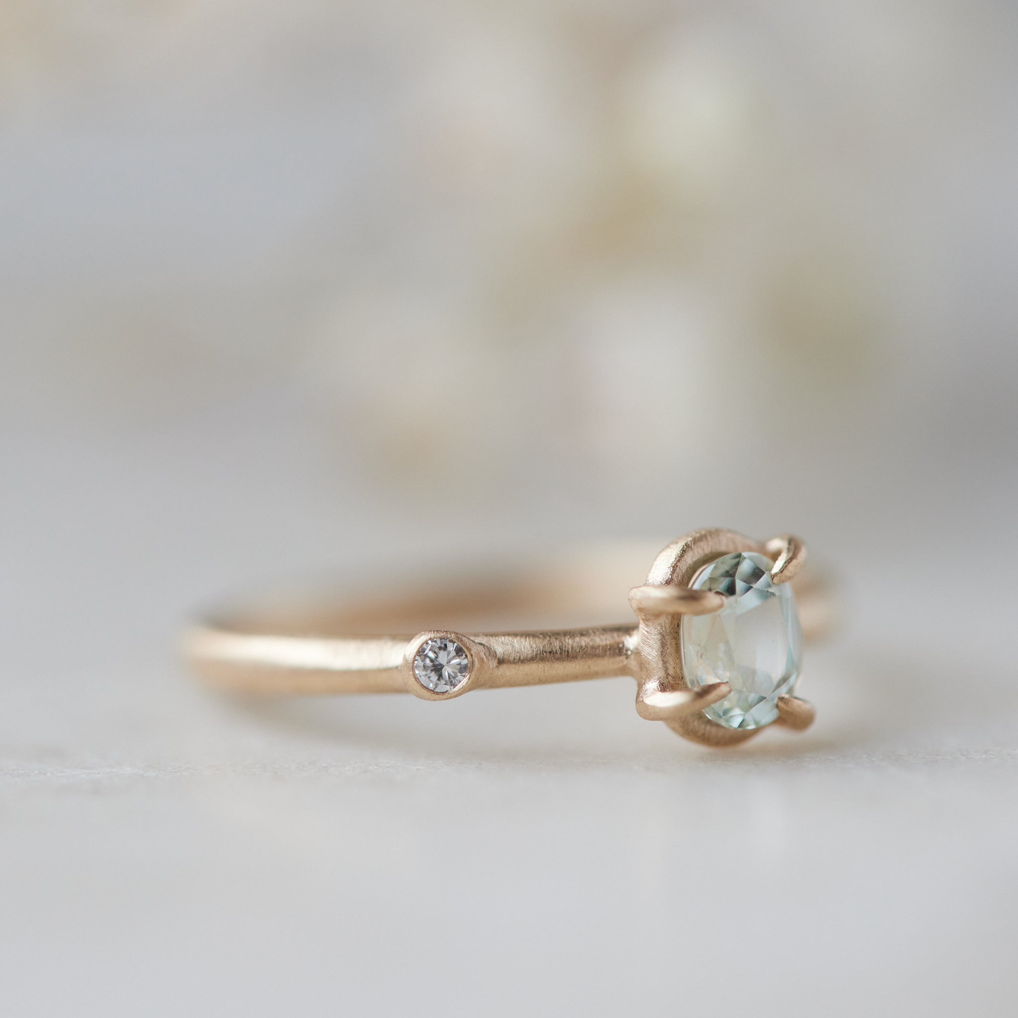 side view of milky clean montana sapphire oval set in a gold ring via a-symetrical prongs and a single diamond accent off-set on the band.