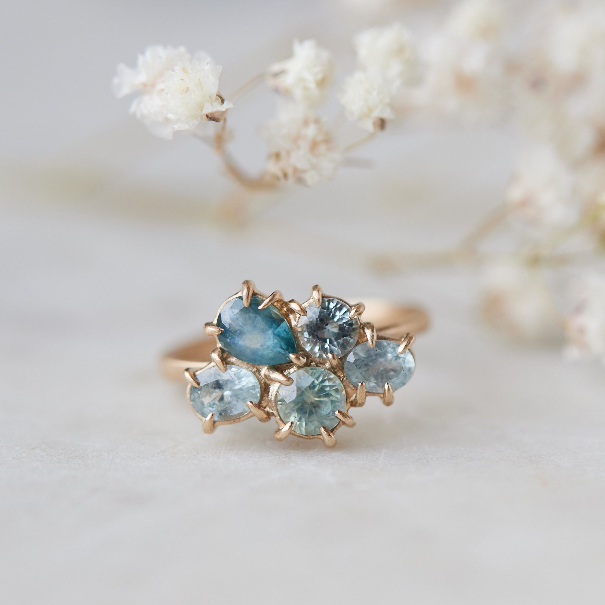 five montana sapphires of various shapes are set in a cluster with gold prongs in a gold ring