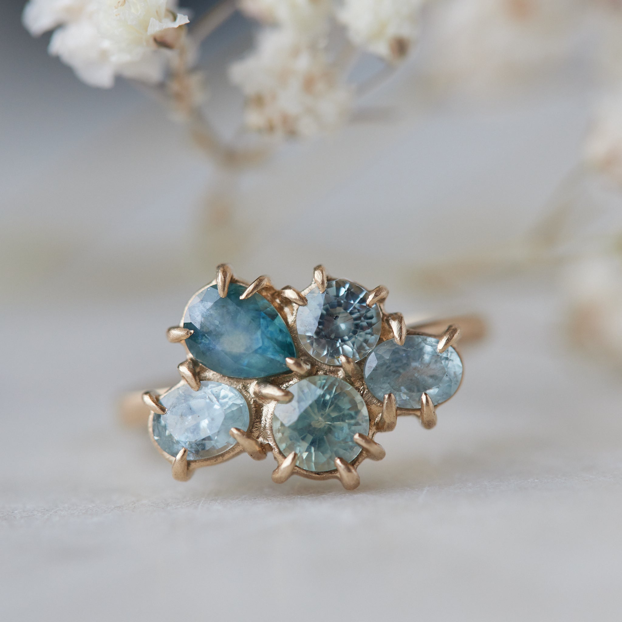 five montana sapphires of various shapes are set in a cluster with gold prongs in a gold ring