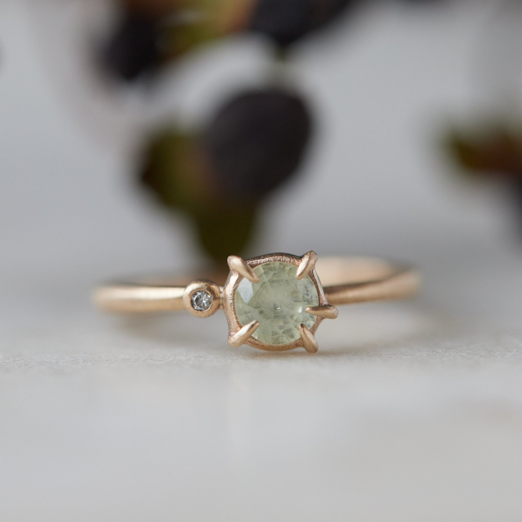 white sapphire set in a gold ring with a single white diamond on the side