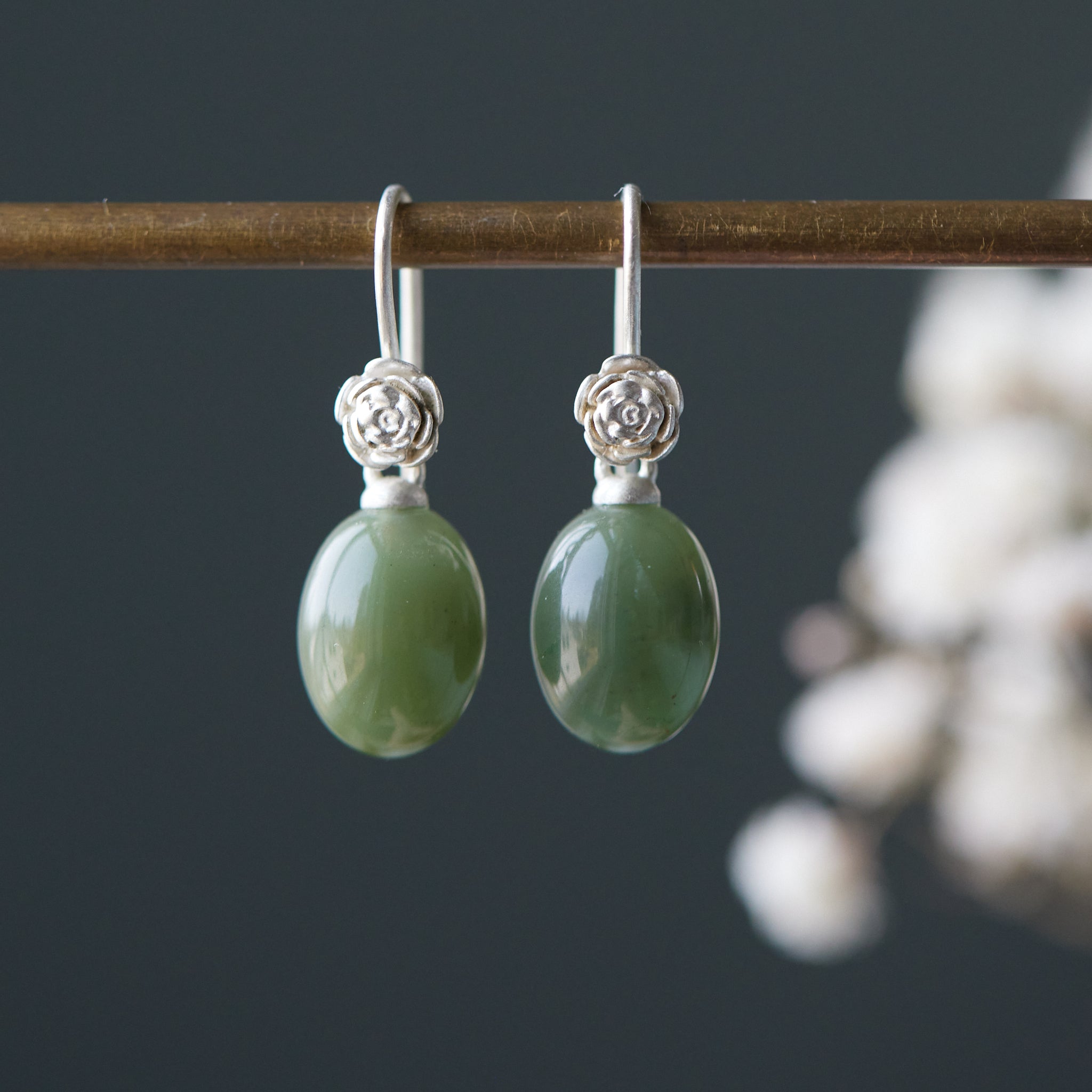 sage green jade oval beads hang beneath silver ear wires featuring little silver roses on them