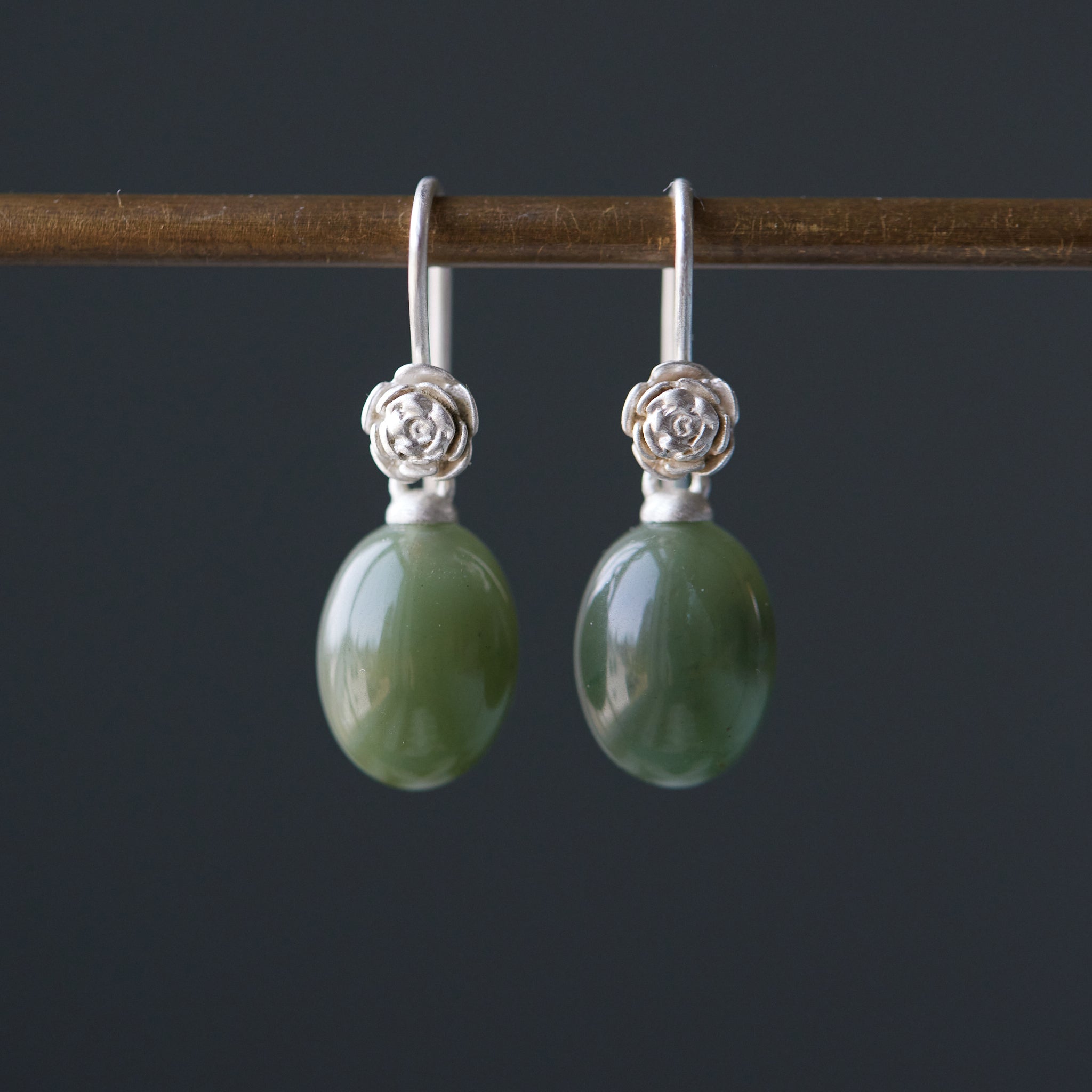 sage green jade oval beads hang beneath silver ear wires featuring little silver roses on them