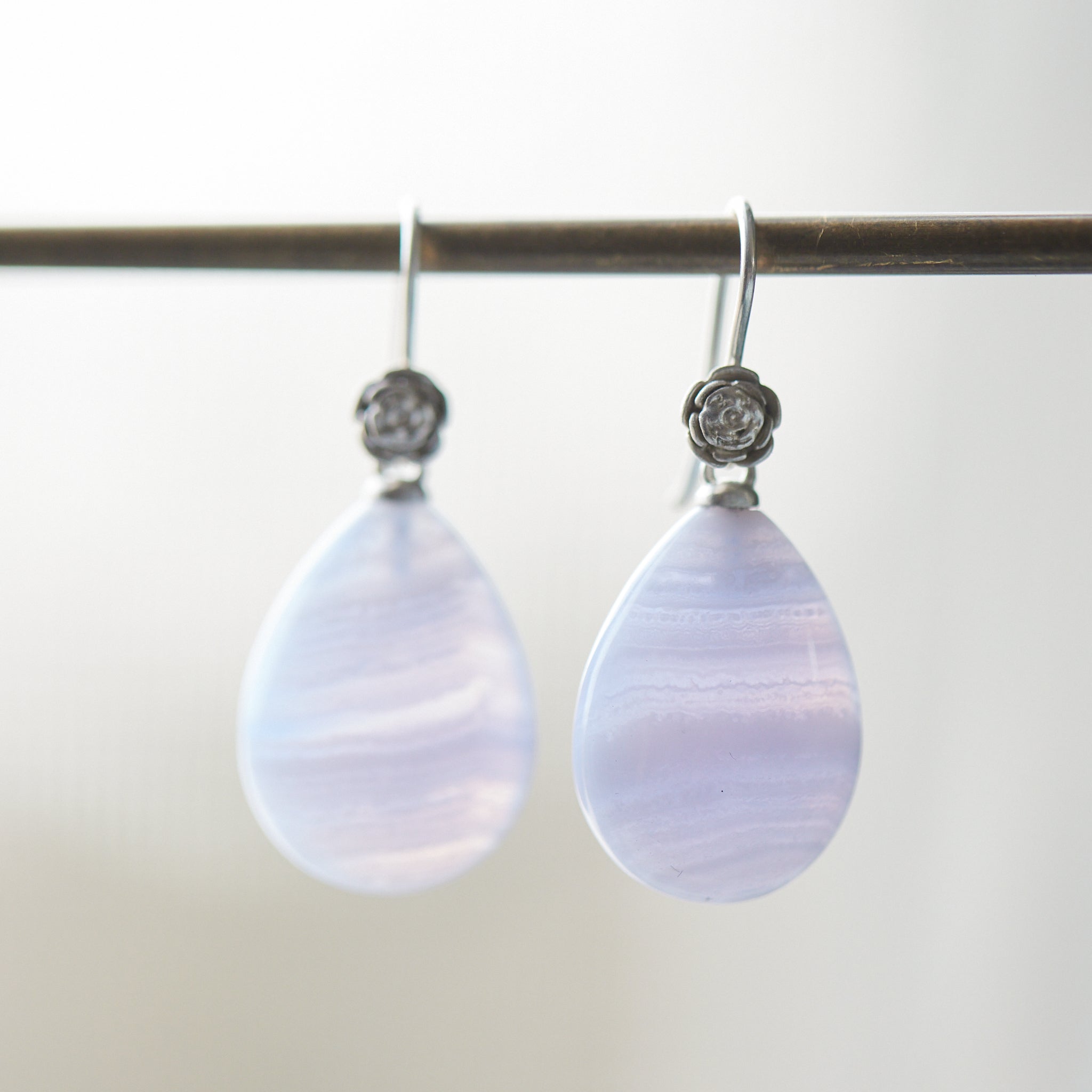 swirly pale blue lace agate teardrops hang beneath silver ear wires featuring little silver roses on them