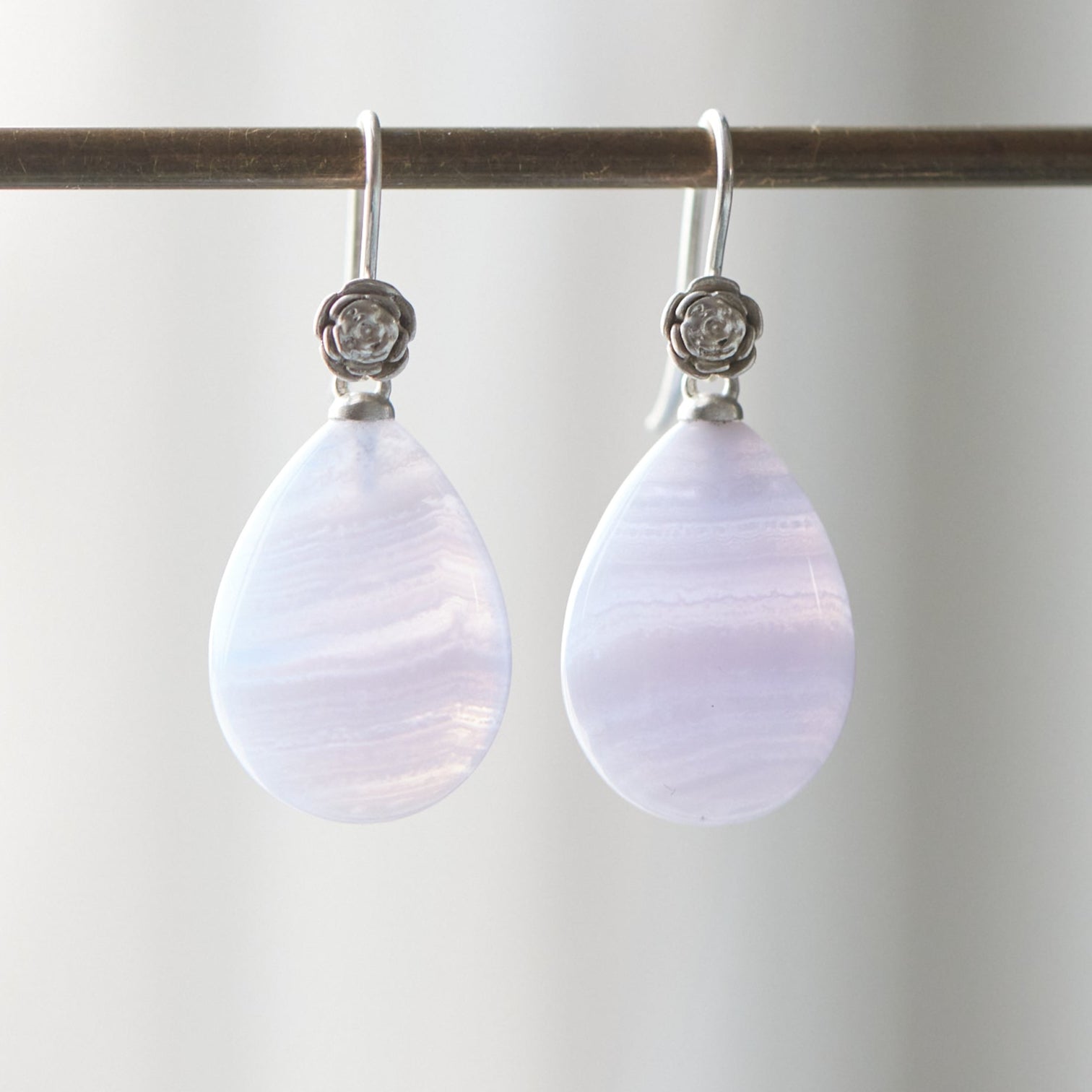 swirly pale blue lace agate teardrops hang beneath silver ear wires featuring little silver roses on them