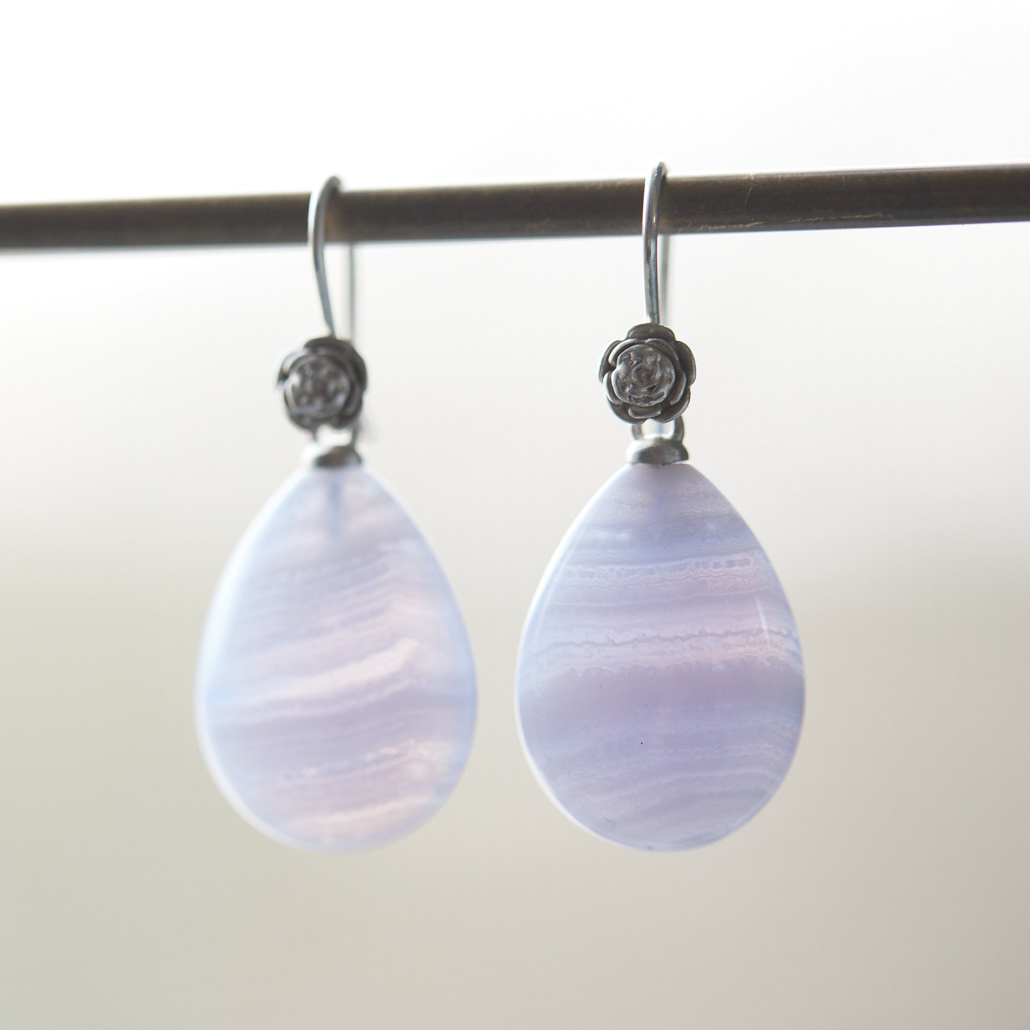 swirly pale blue lace agate teardrops hang beneath silver ear wires featuring little silver roses on them