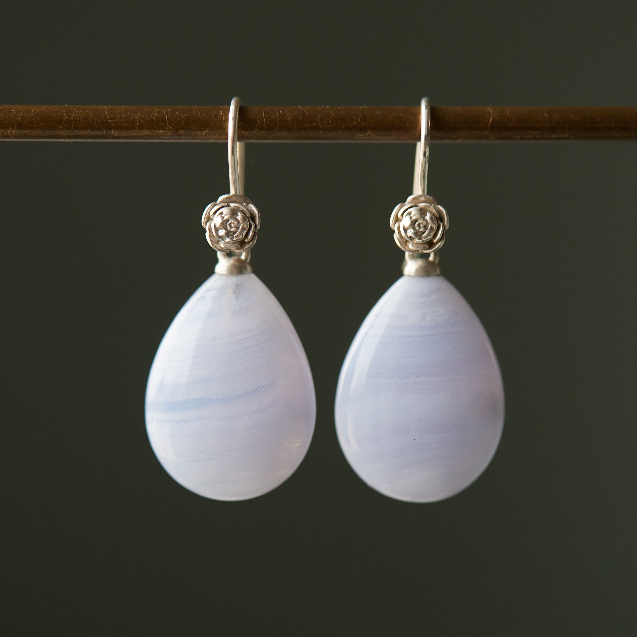 swirly pale blue lace agate teardrops hang beneath silver ear wires featuring little silver roses on them