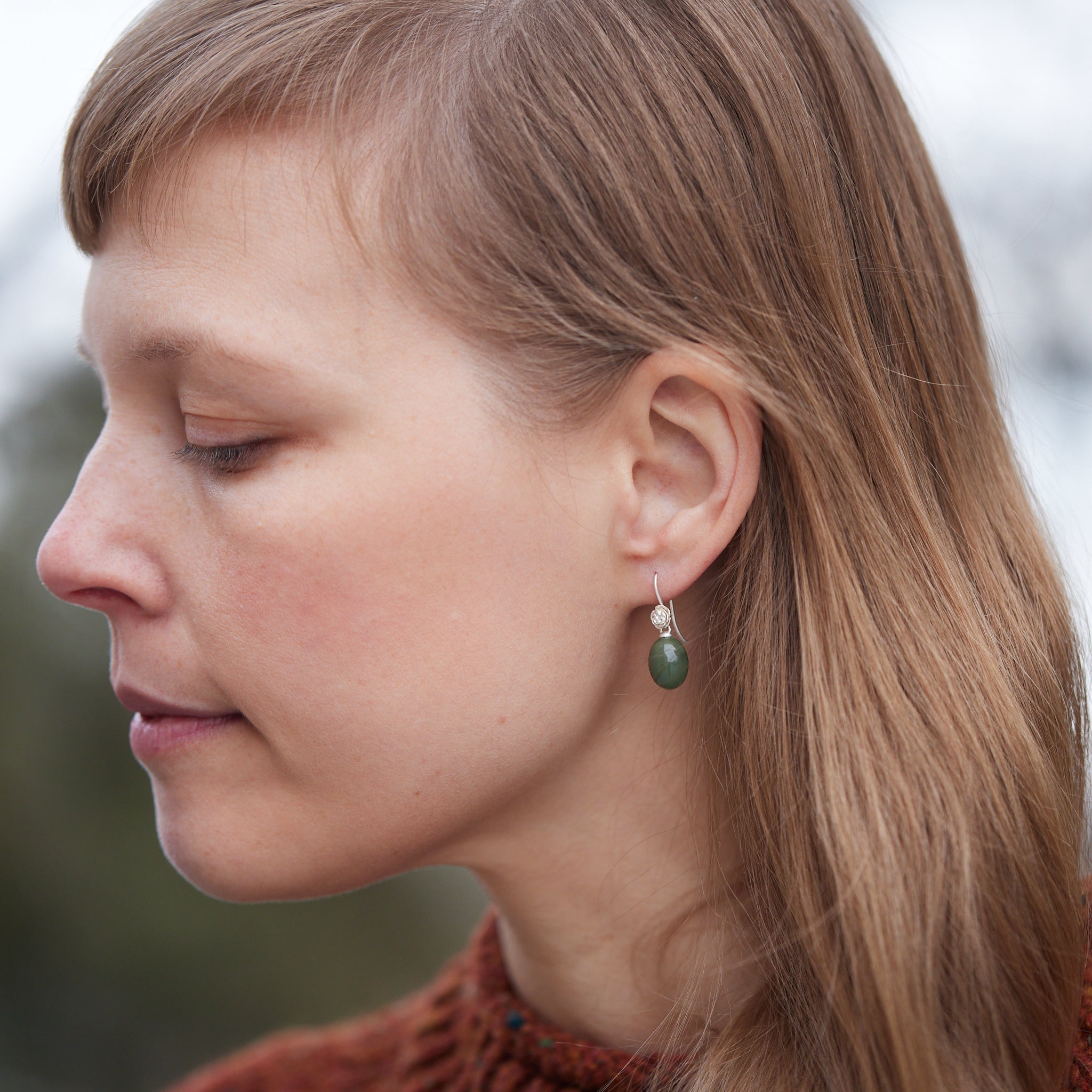 sage green jade oval beads hang beneath silver ear wires featuring little silver roses on them