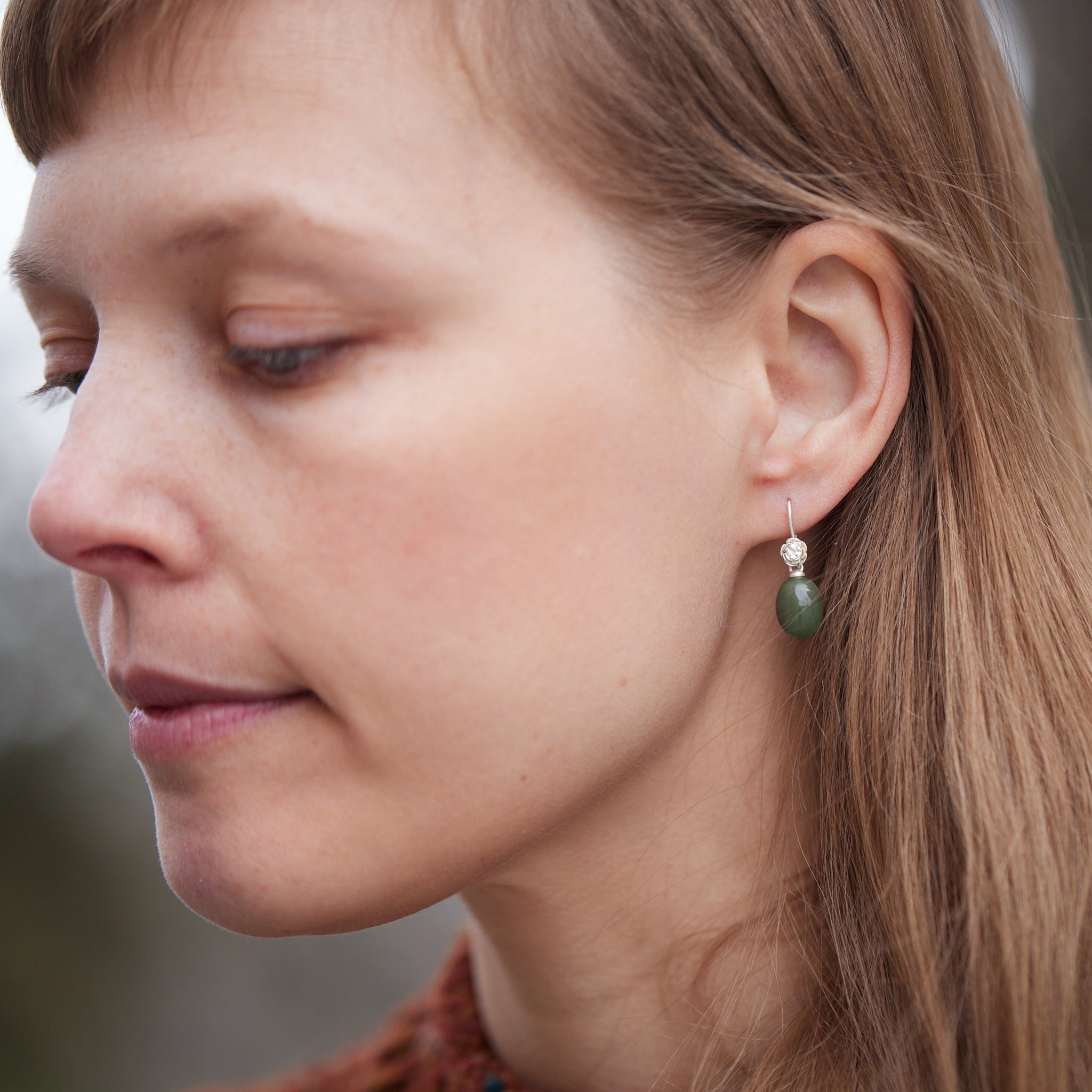 sage green jade oval beads hang beneath silver ear wires featuring little silver roses on them