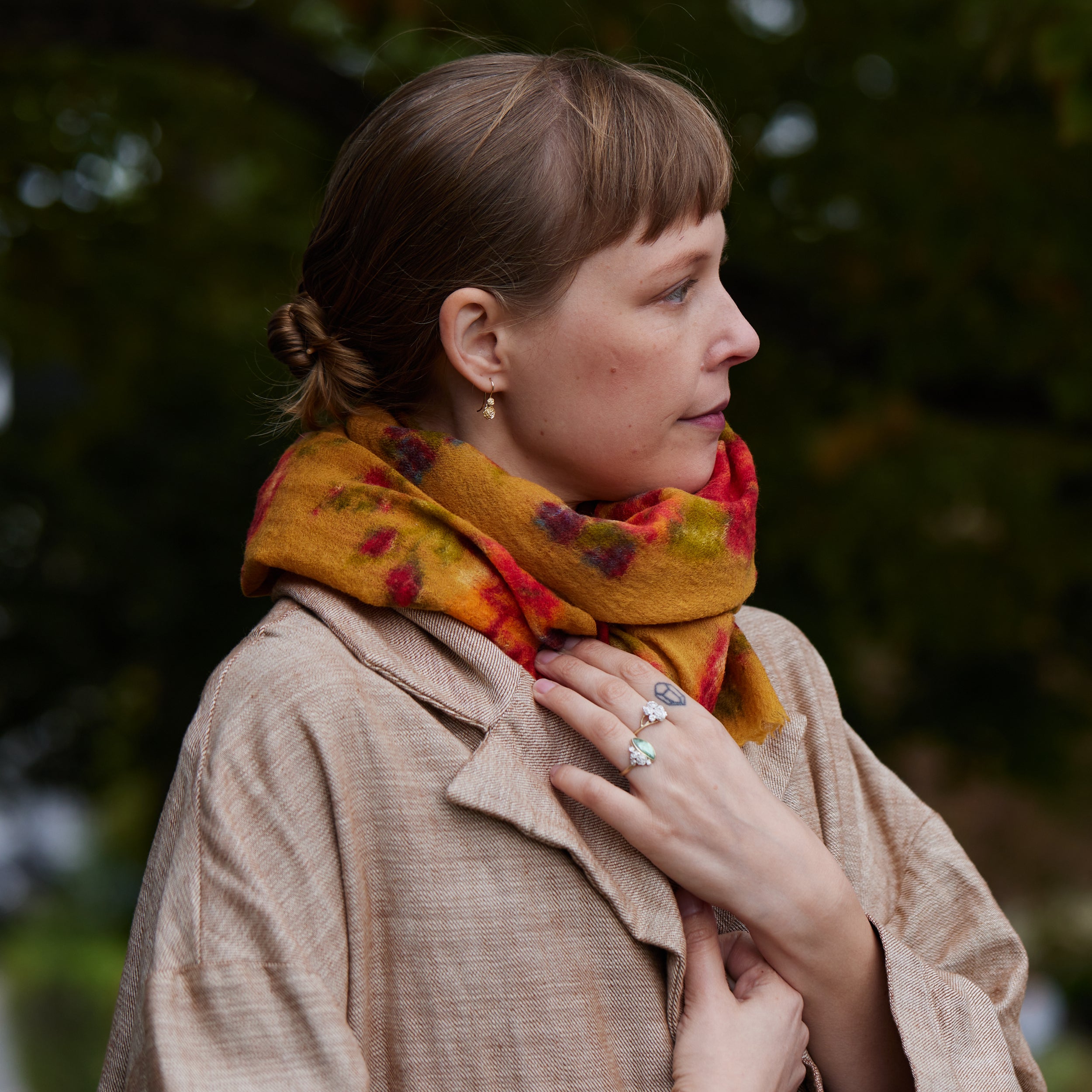 girl wearing double rose garden drop earrings and a scar and jacket. She is also wearing two rings. trees are behind her.