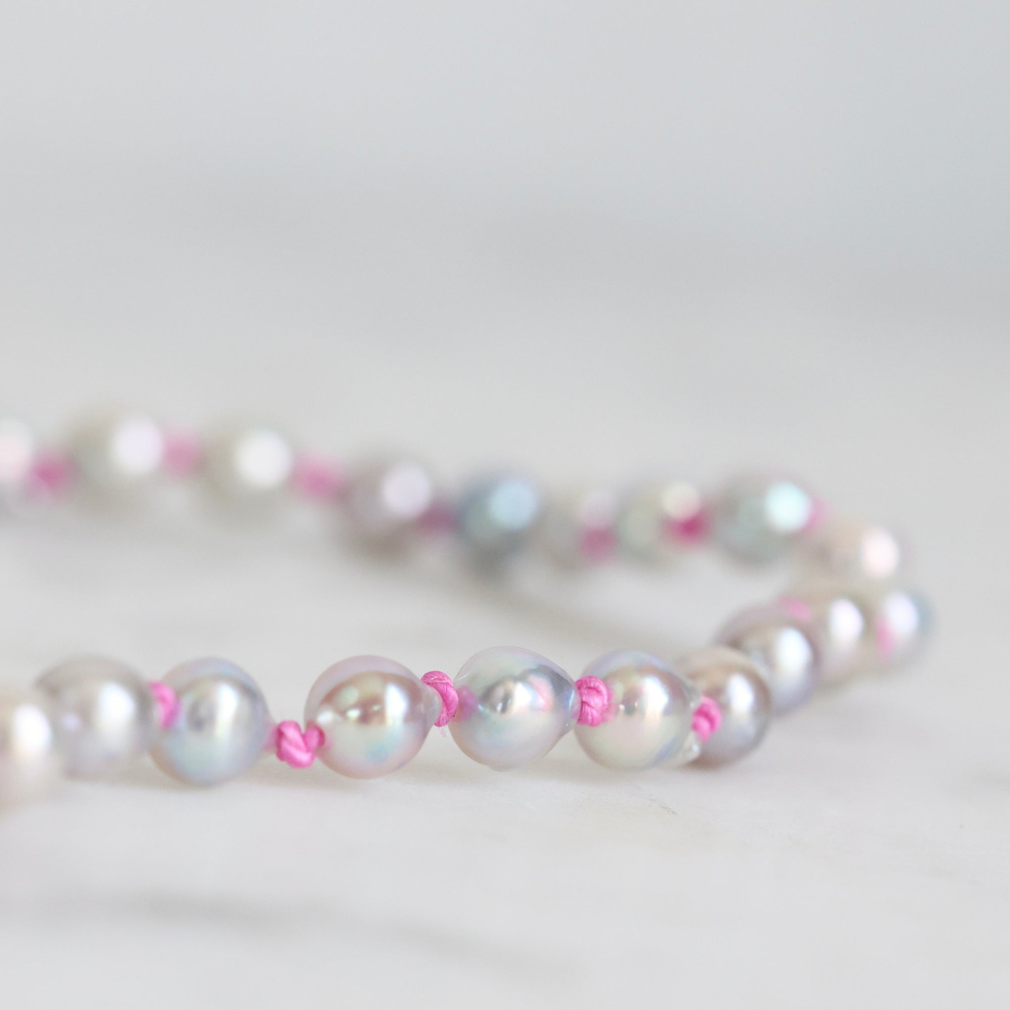 Pearl necklace with pink accents on a light gray background