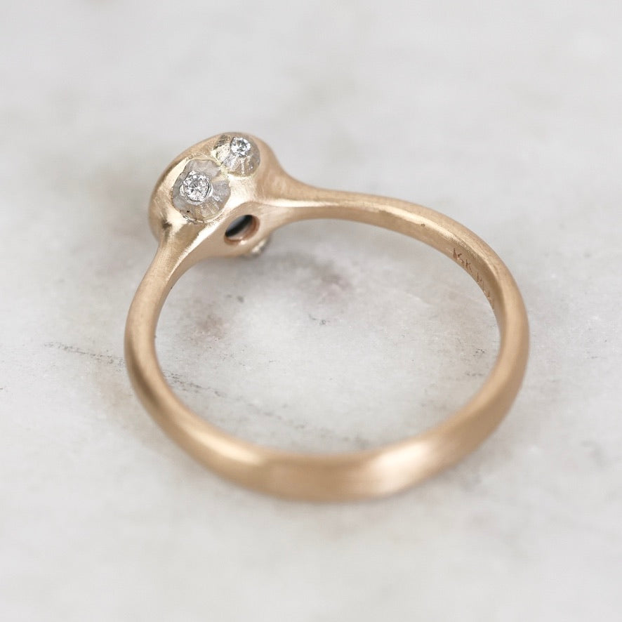 A close-up of a rose gold ring with a unique split-band design and two small clear gemstones, resting on a light marble surface.