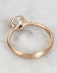 A close-up of a rose gold ring with a unique split-band design and two small clear gemstones, resting on a light marble surface.