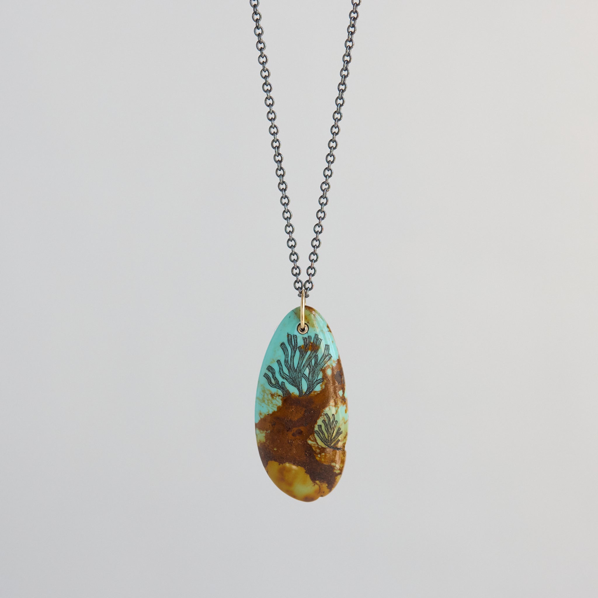 Necklace with a pendant featuring a seaweed design on a light gray background