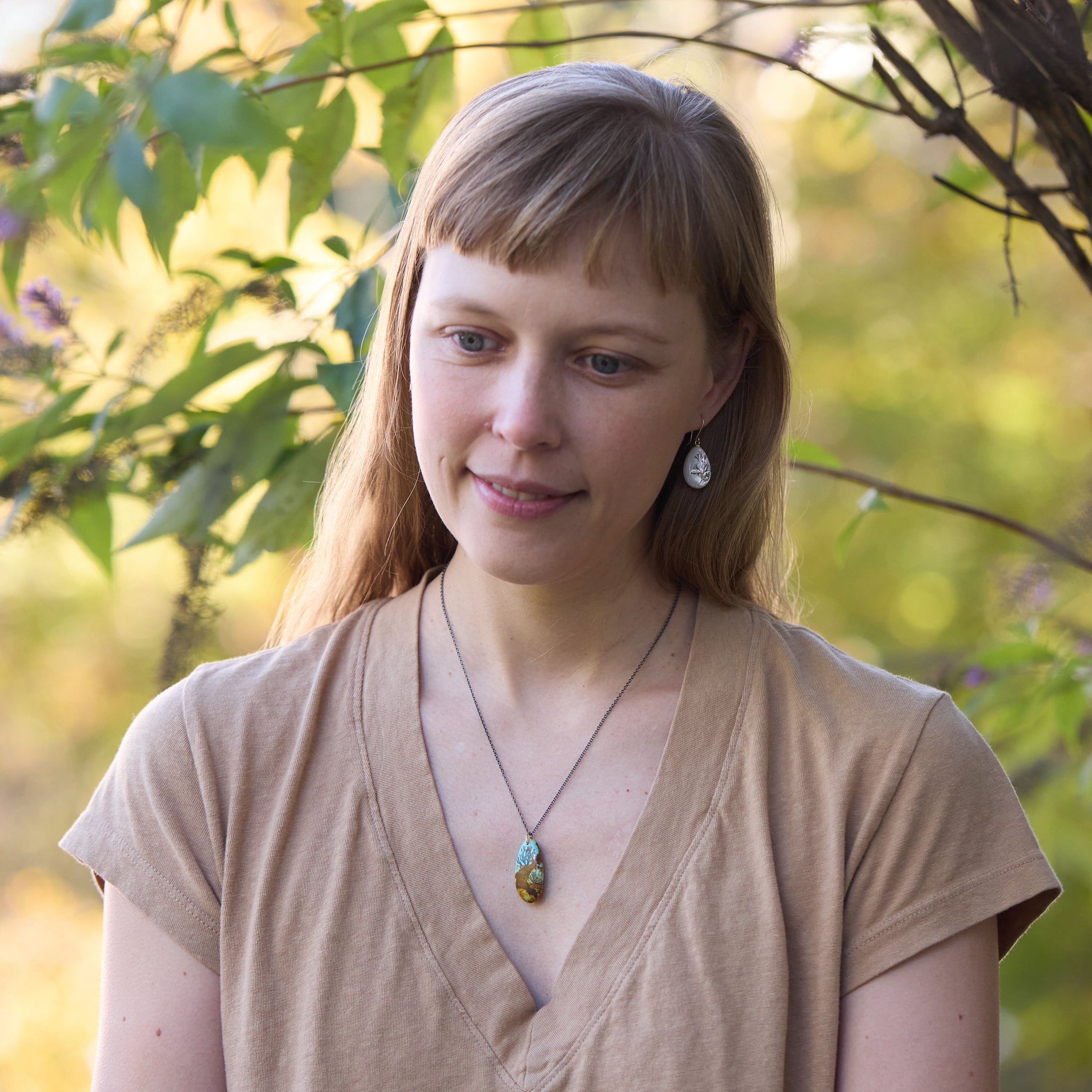 Woman with a necklace standing outdoors with greenery in the background