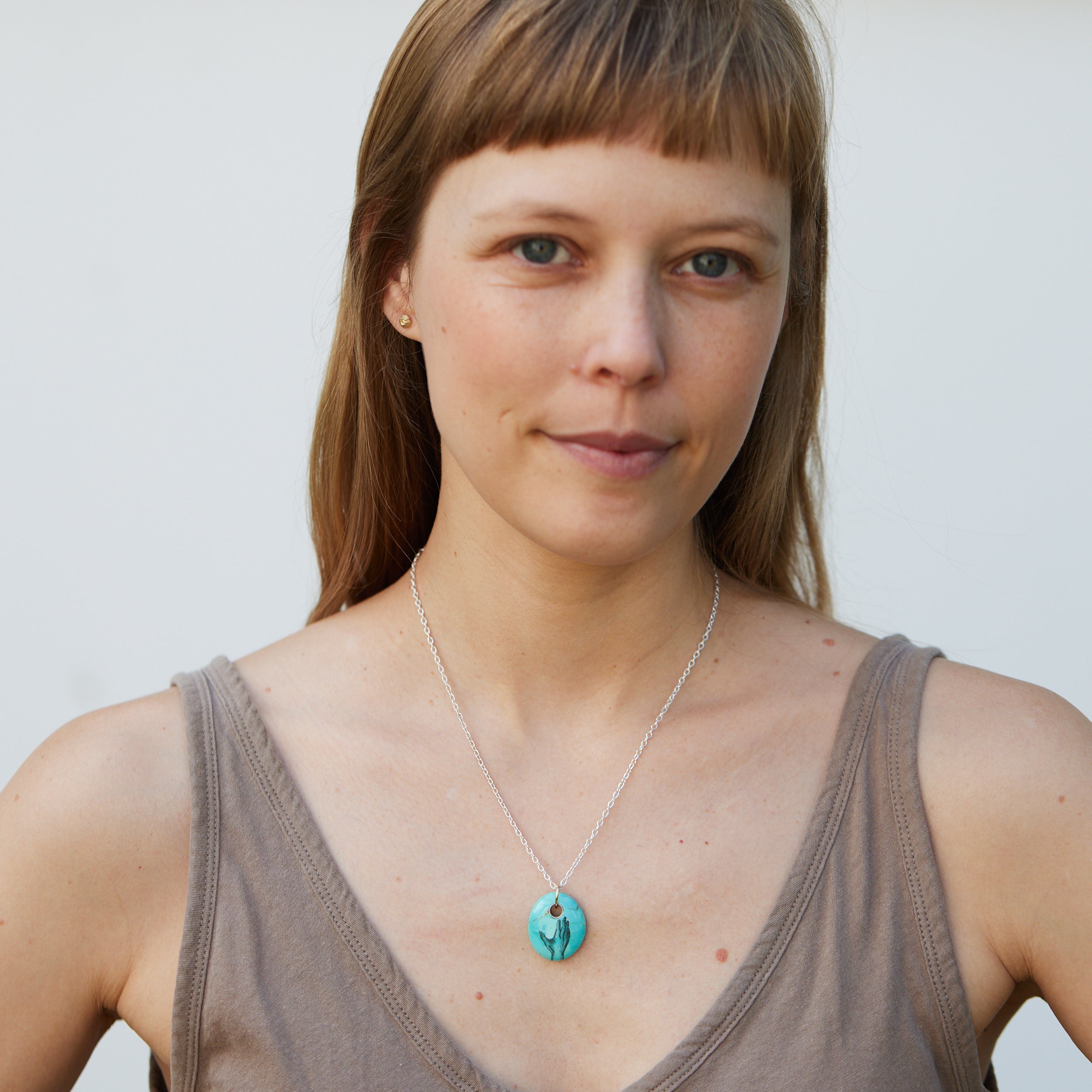 kingman turquoise bead pendant necklace on silver chain with gold bail. A scrimshaw hand is inked to the front.