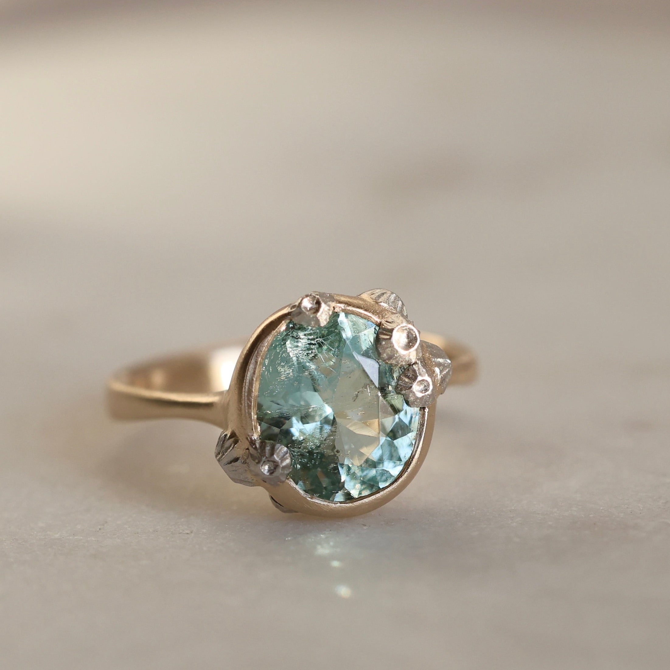 Gold ring with a green gemstone on a neutral background