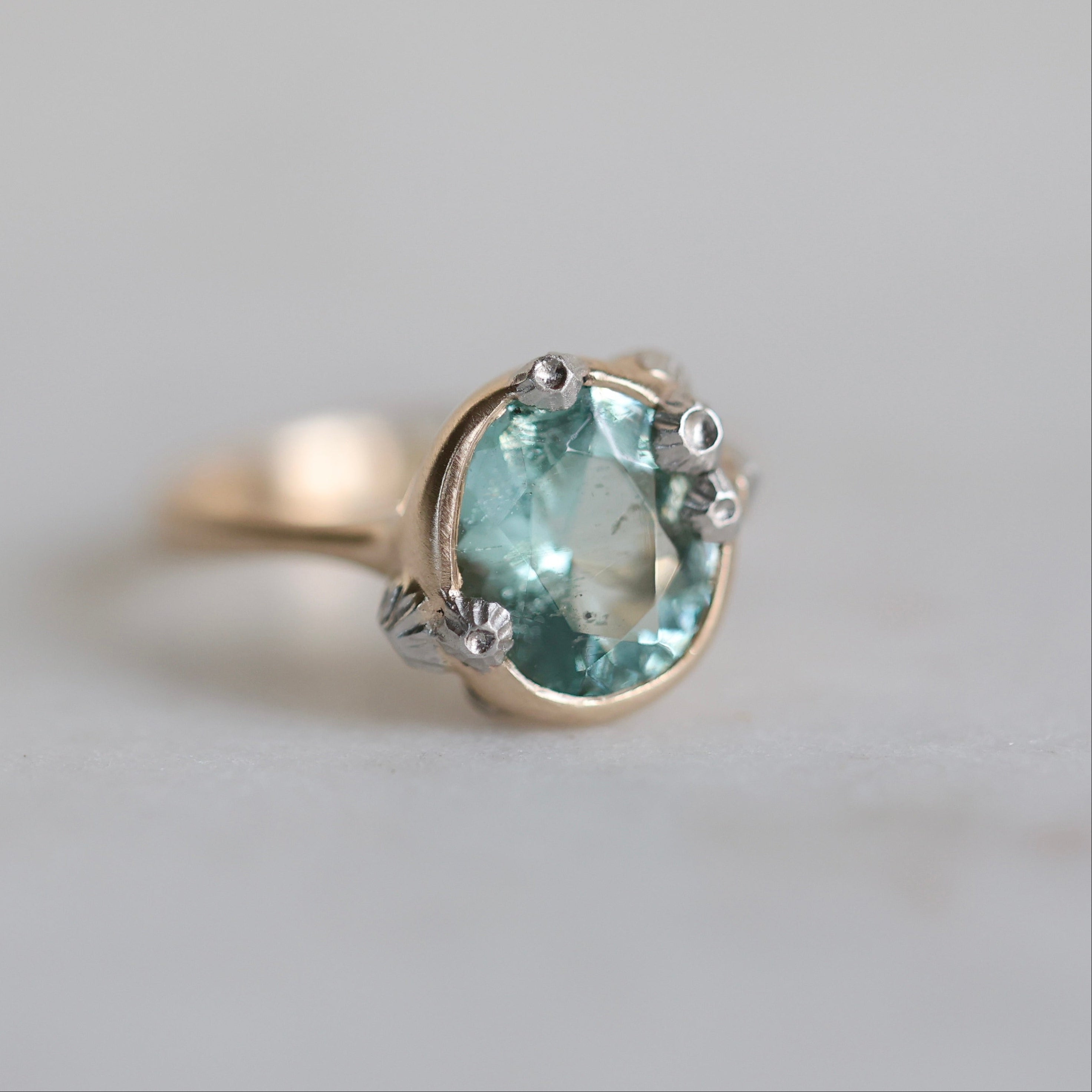 Ring with a green gemstone and gold band on a light gray background