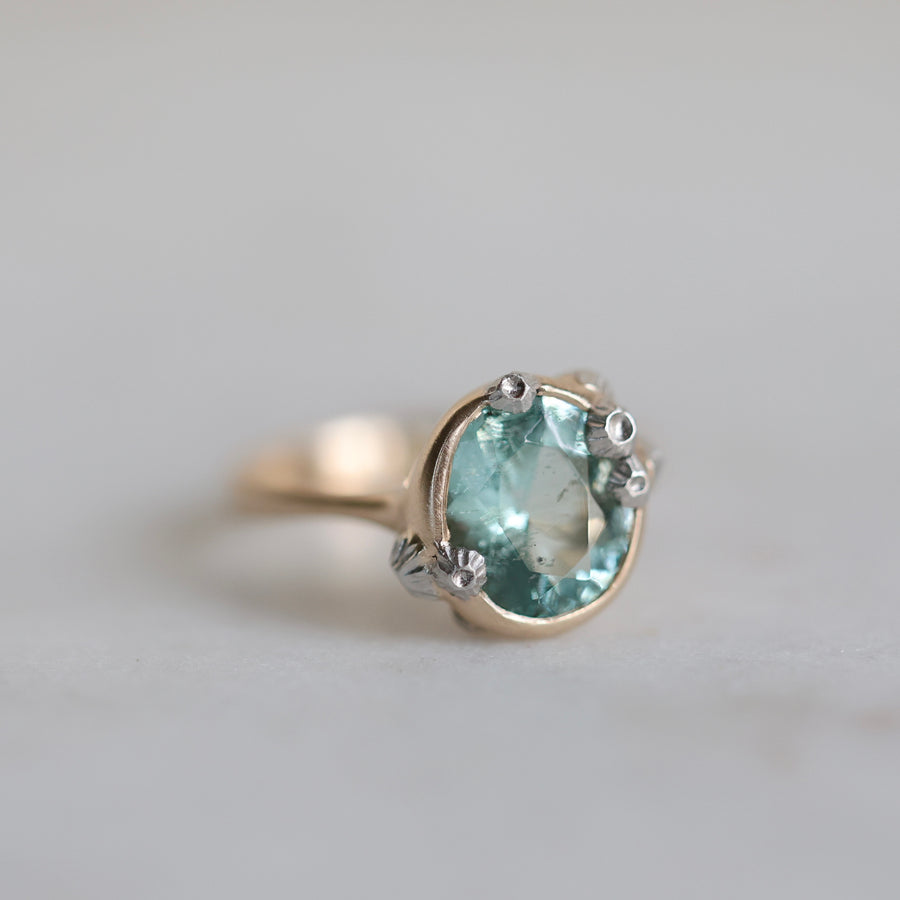 Ring with a green gemstone and gold band on a light gray background