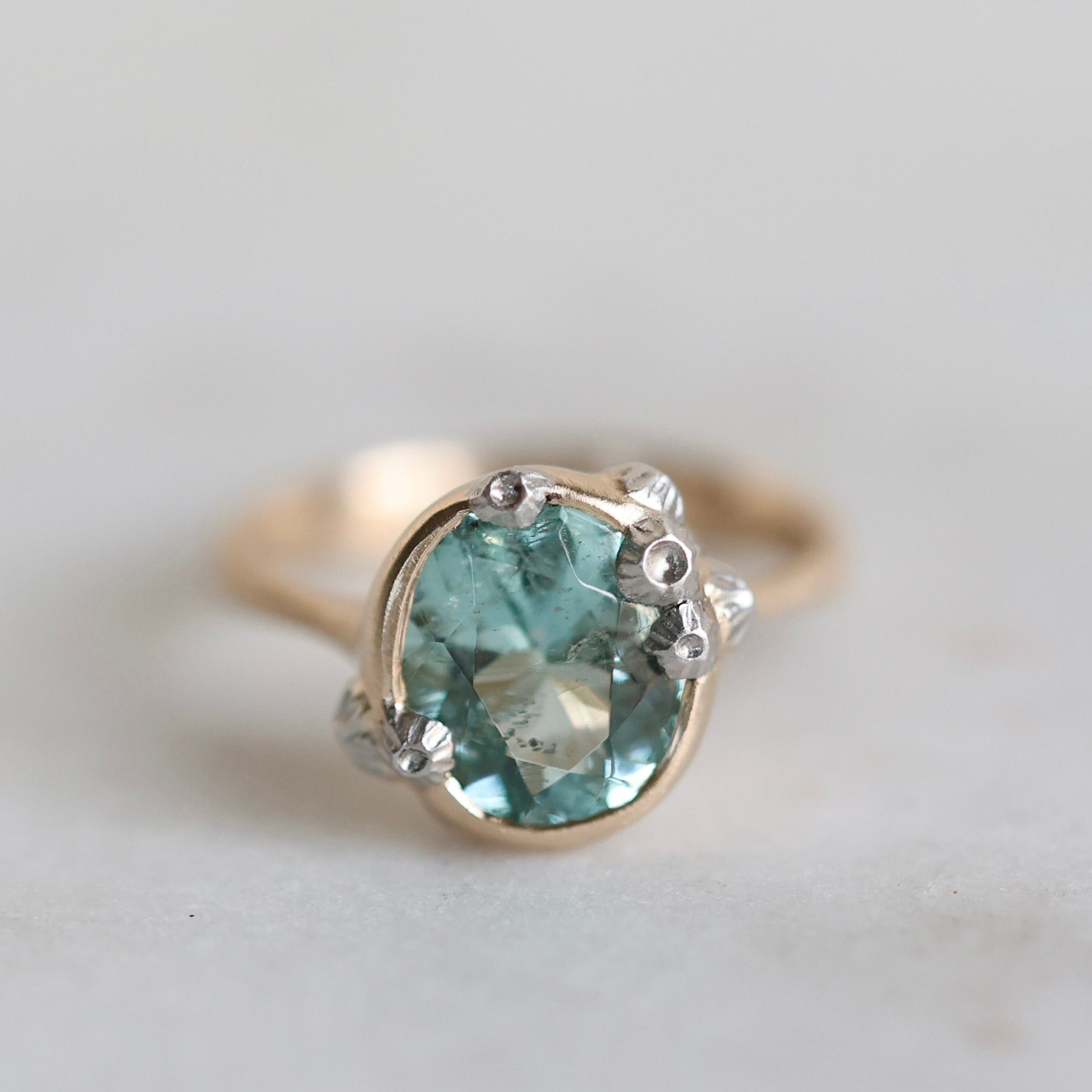 Gold ring with a green gemstone on a light gray background