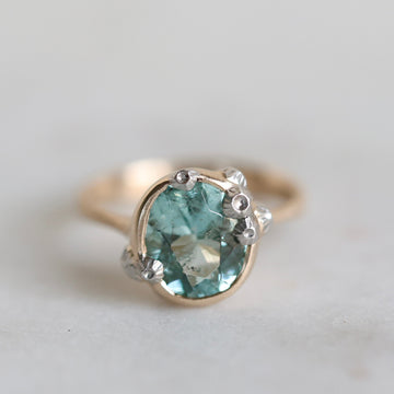Gold ring with a green gemstone on a light gray background