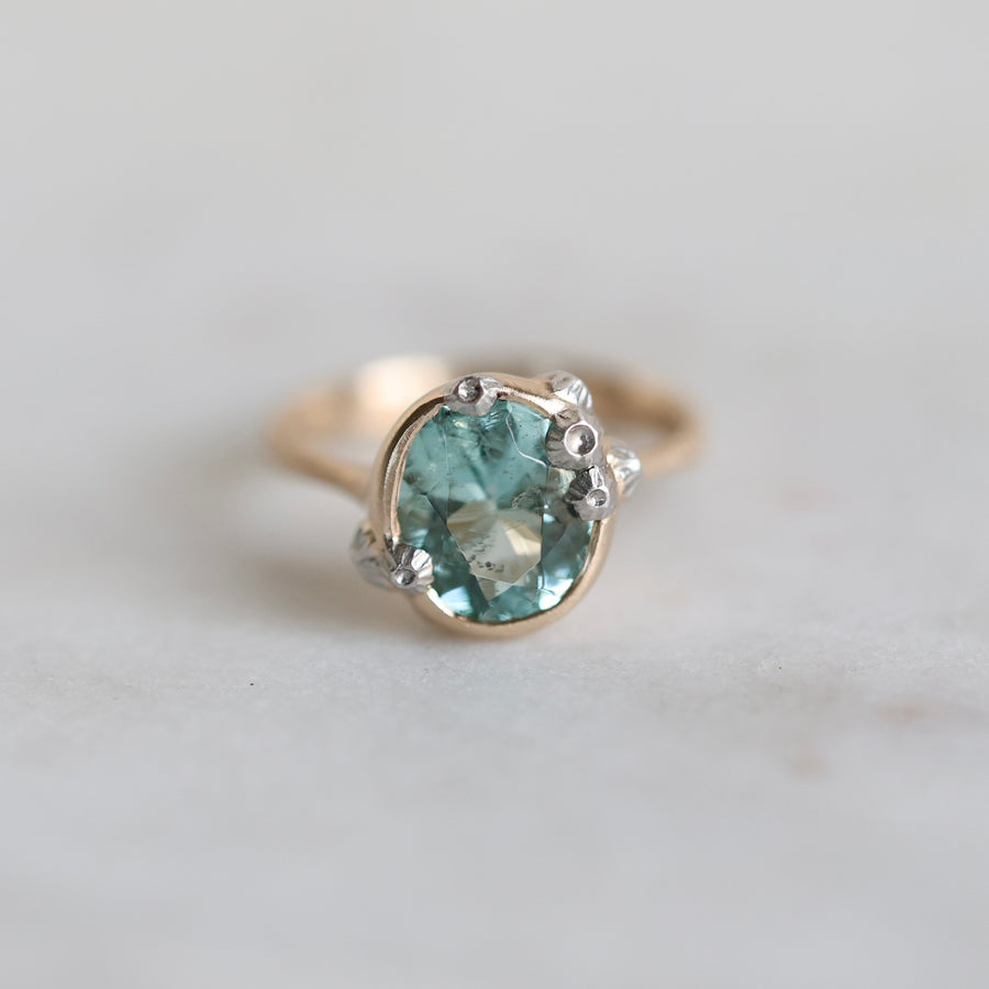 Gold ring with a green gemstone on a light gray background