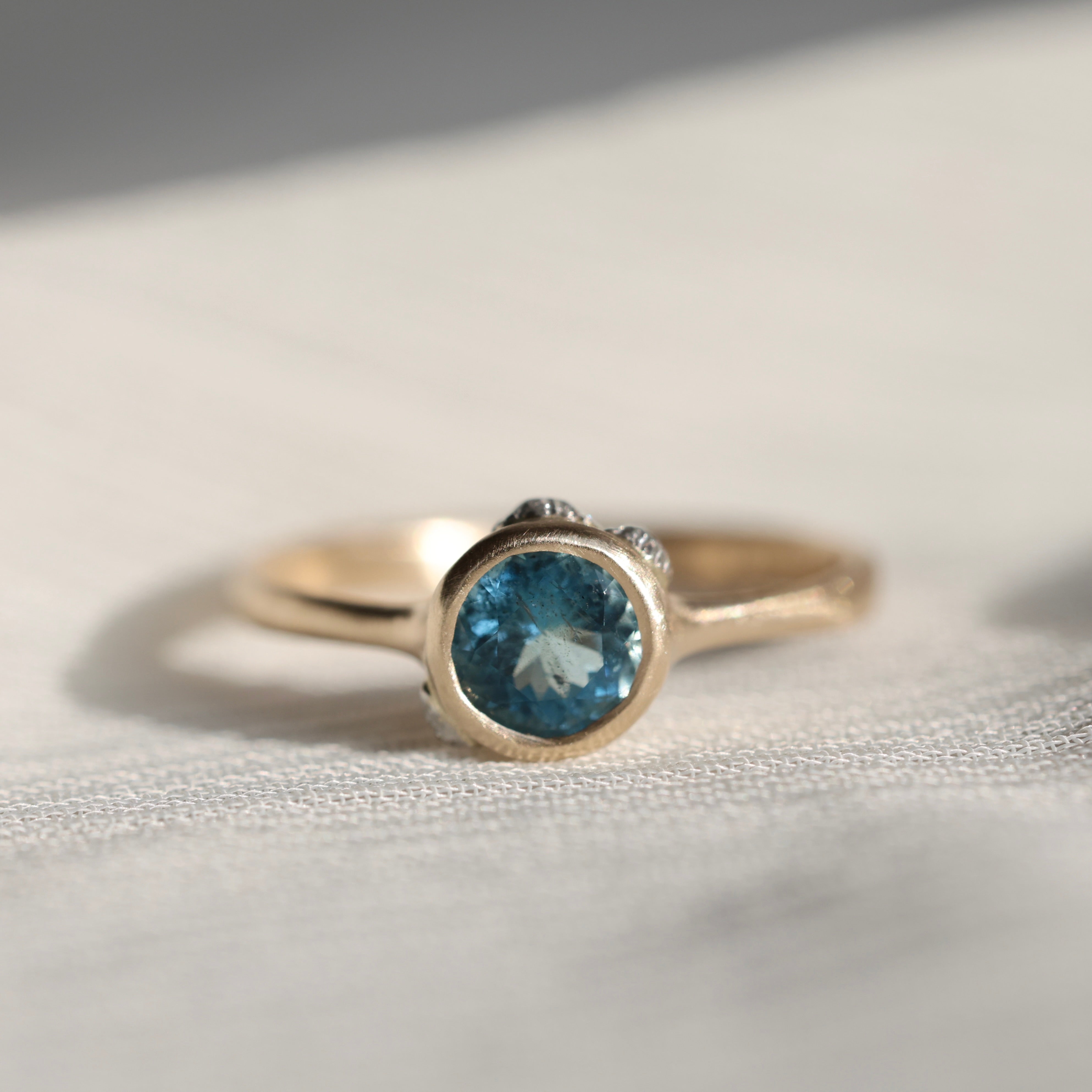 gold ring with blue stone on a pale fabric surface
