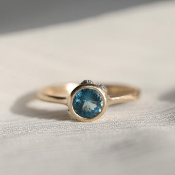 gold ring with blue stone on a pale fabric surface