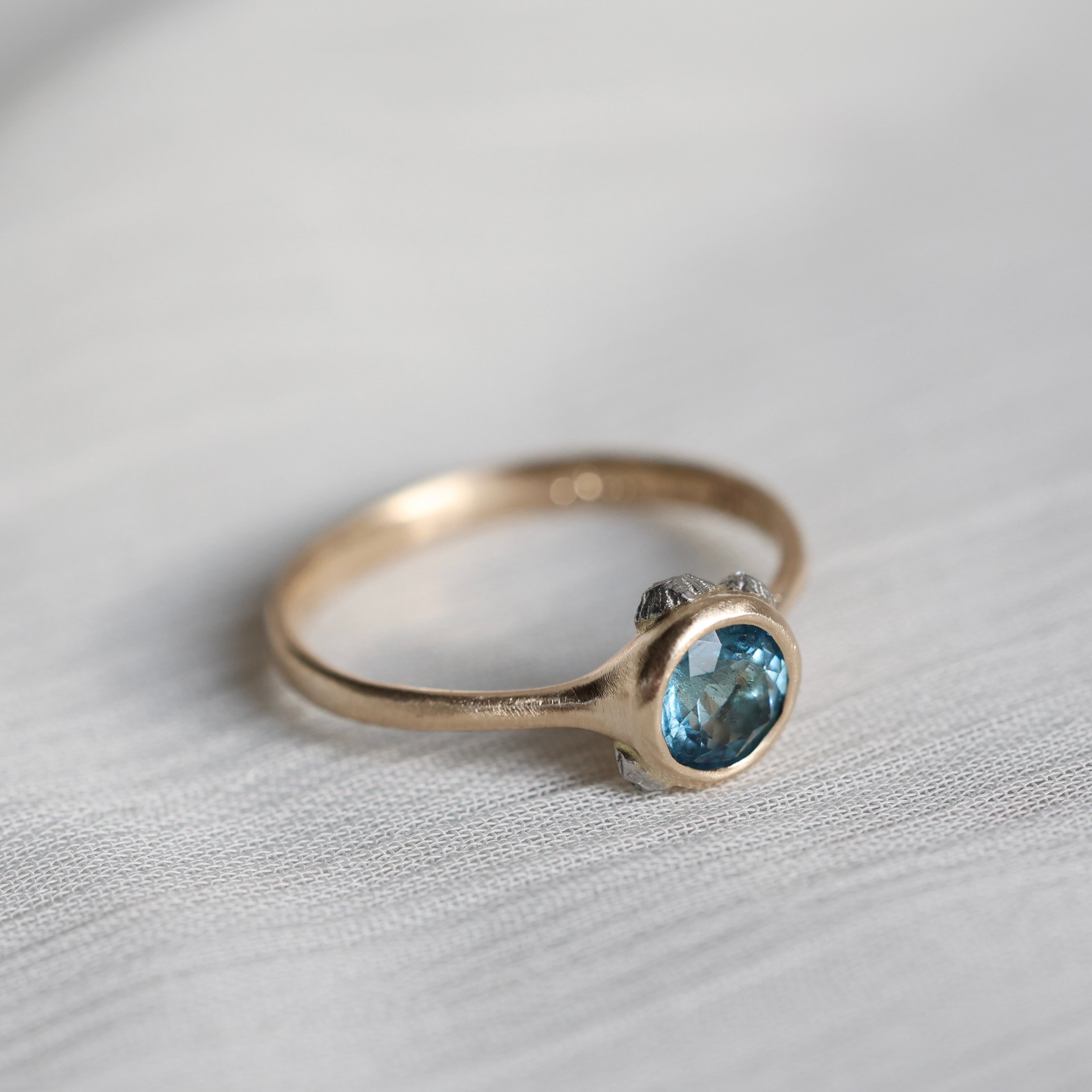 gold ring with blue stone on a pale fabric surface