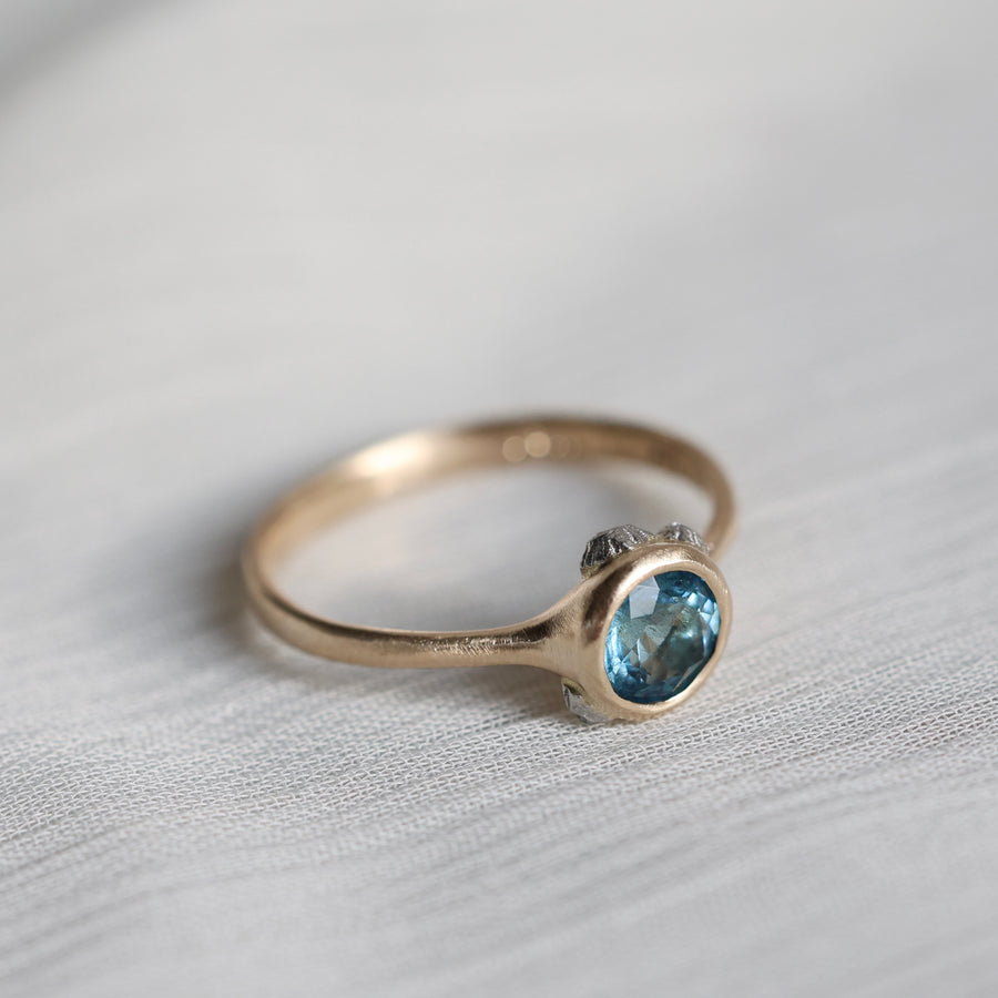 gold ring with blue stone on a pale fabric surface
