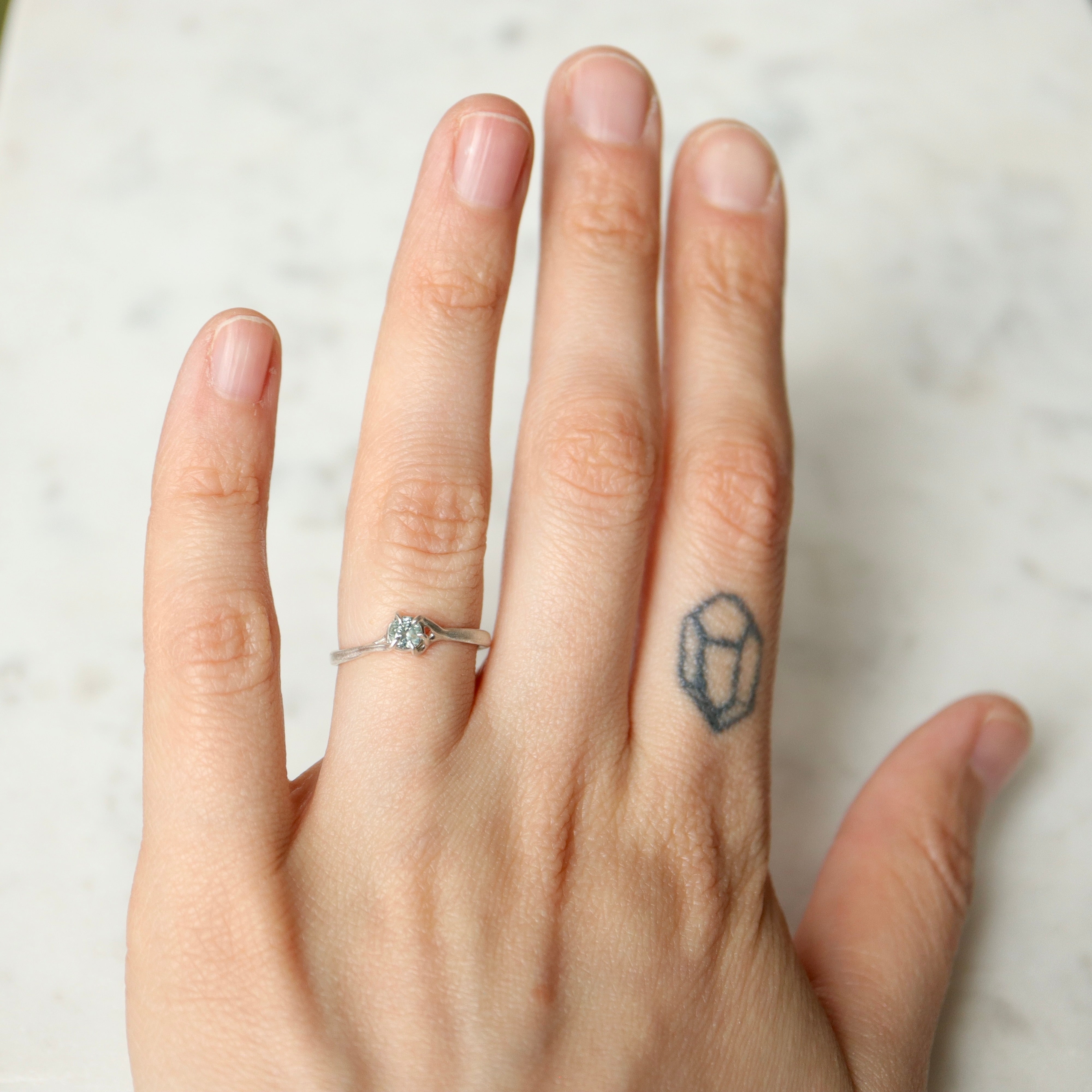 on-hand view of a round pale blue montana sapphire set in a silver ring. The stone is wrapped in branching prongs. Shown on a white marble slab.