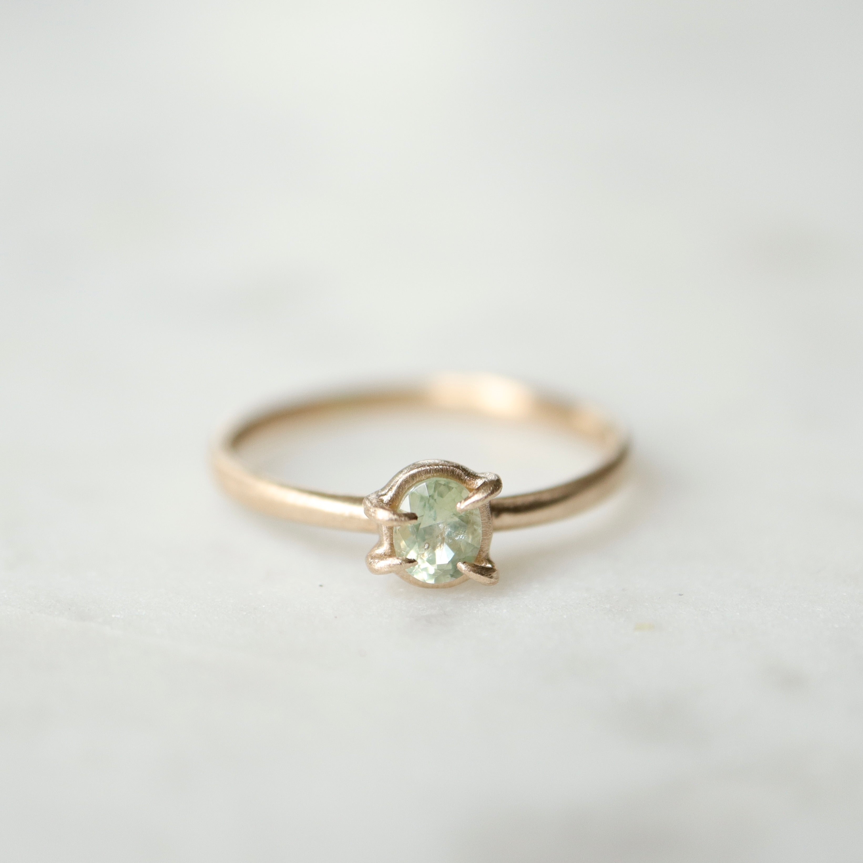 an oval pale aloe green montana sapphire is set in a gold ring within a-symmetrial gold prongs