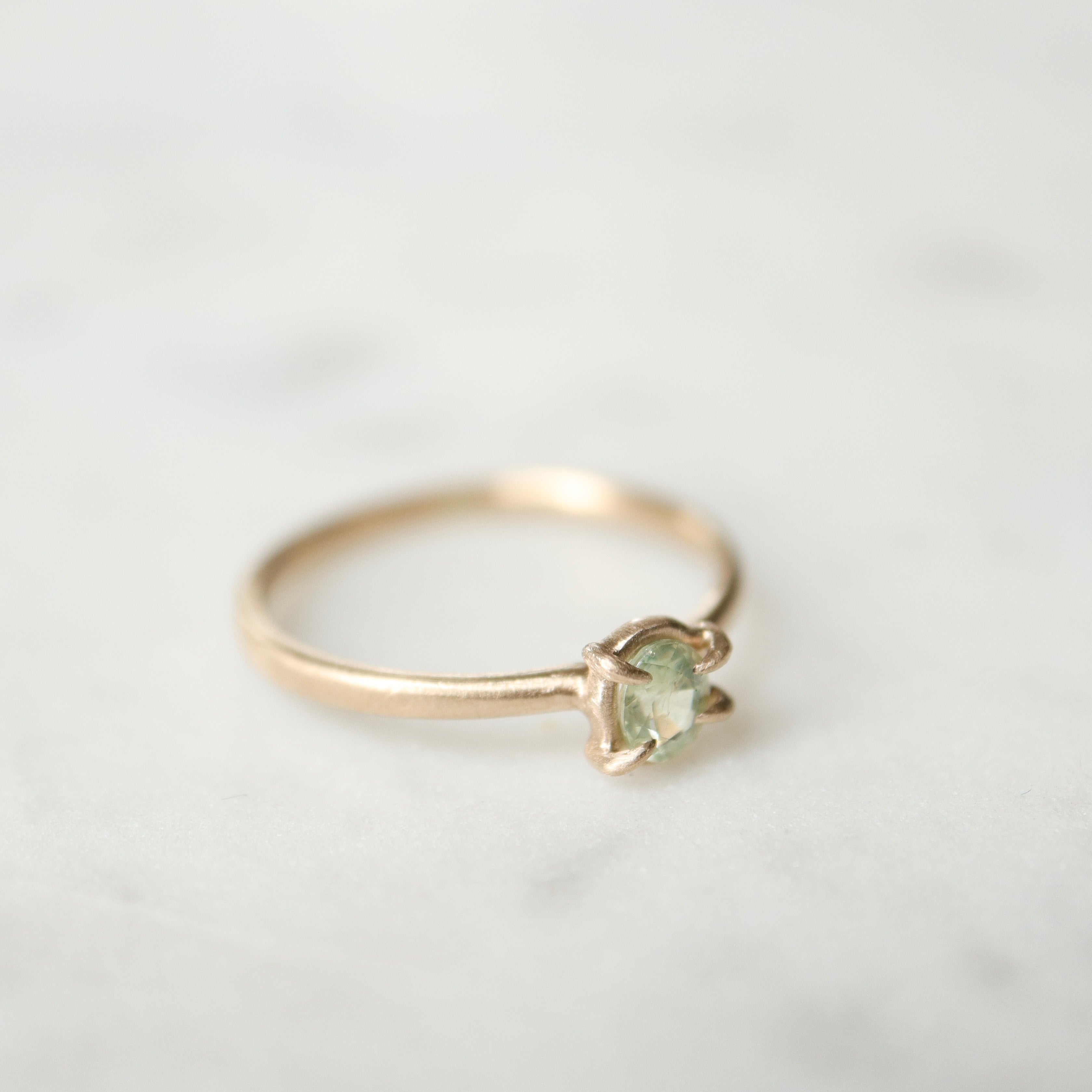 side view of an oval pale aloe green montana sapphire is set in a gold ring within a-symmetrial gold prongs