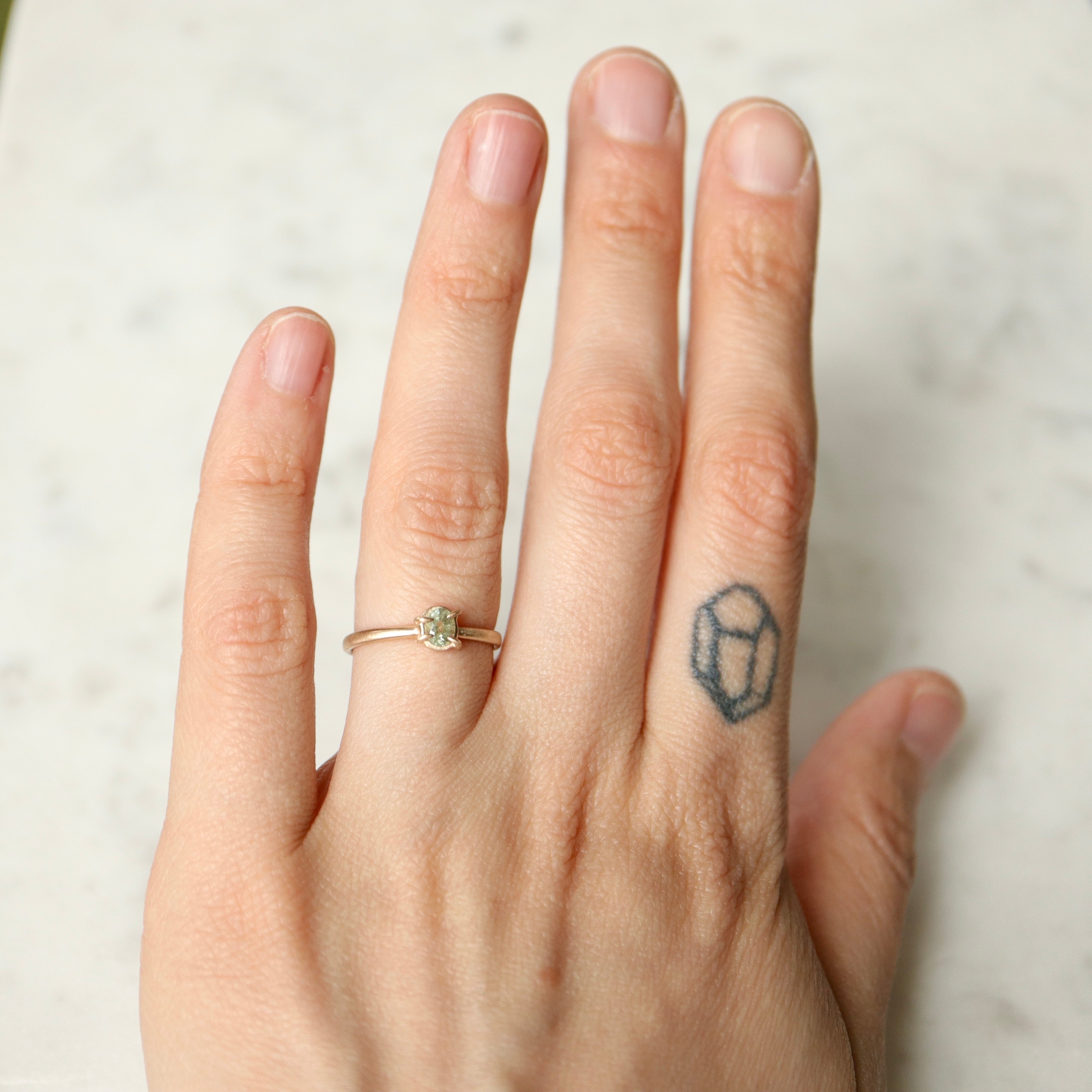 an oval pale aloe green montana sapphire is set in a gold ring within a-symmetrial gold prongs- shown on hand