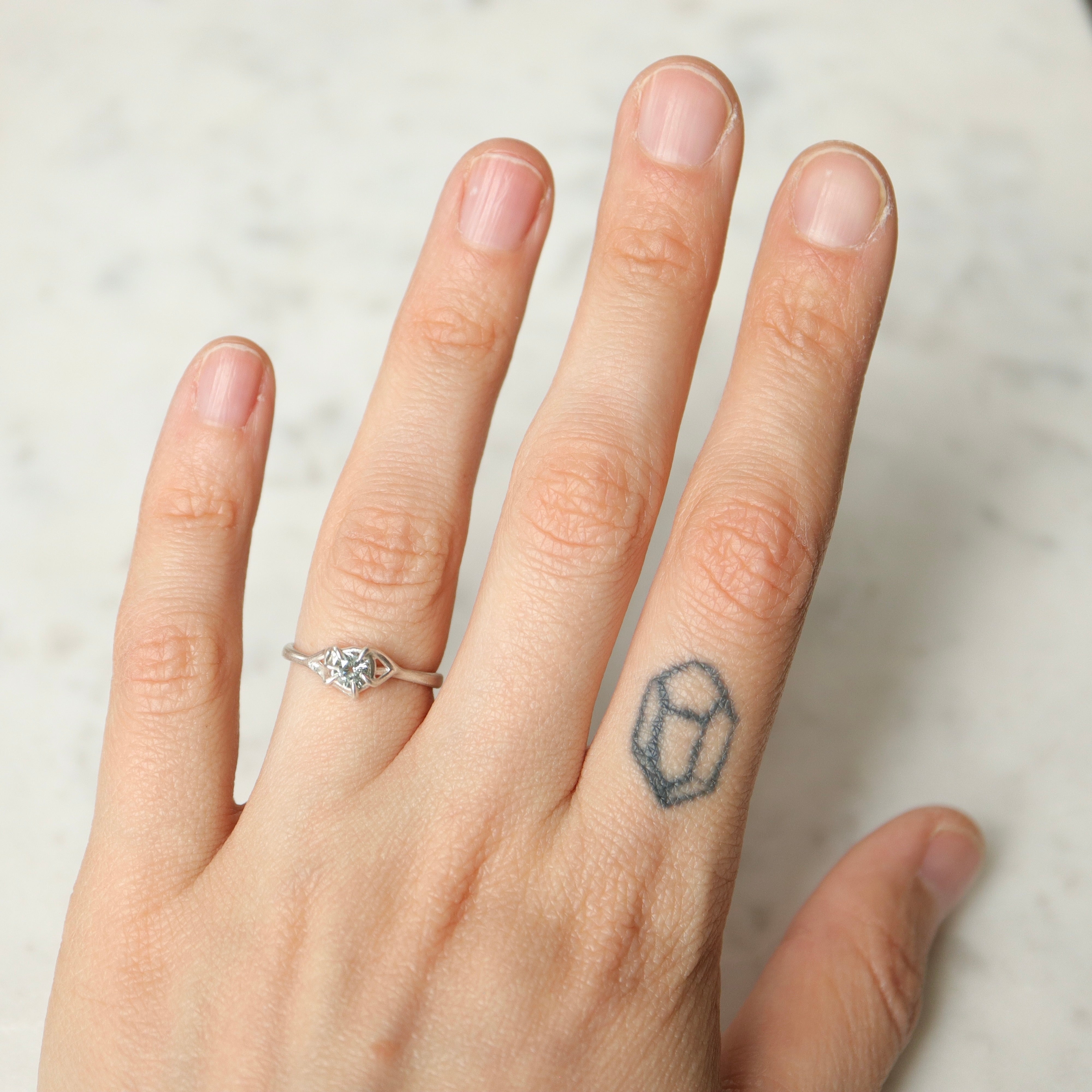 On-hand view of a round, pale blue montana sapphire set in a silver ring. The stone is wrapped in branching prongs and photographed on a white marble slab.