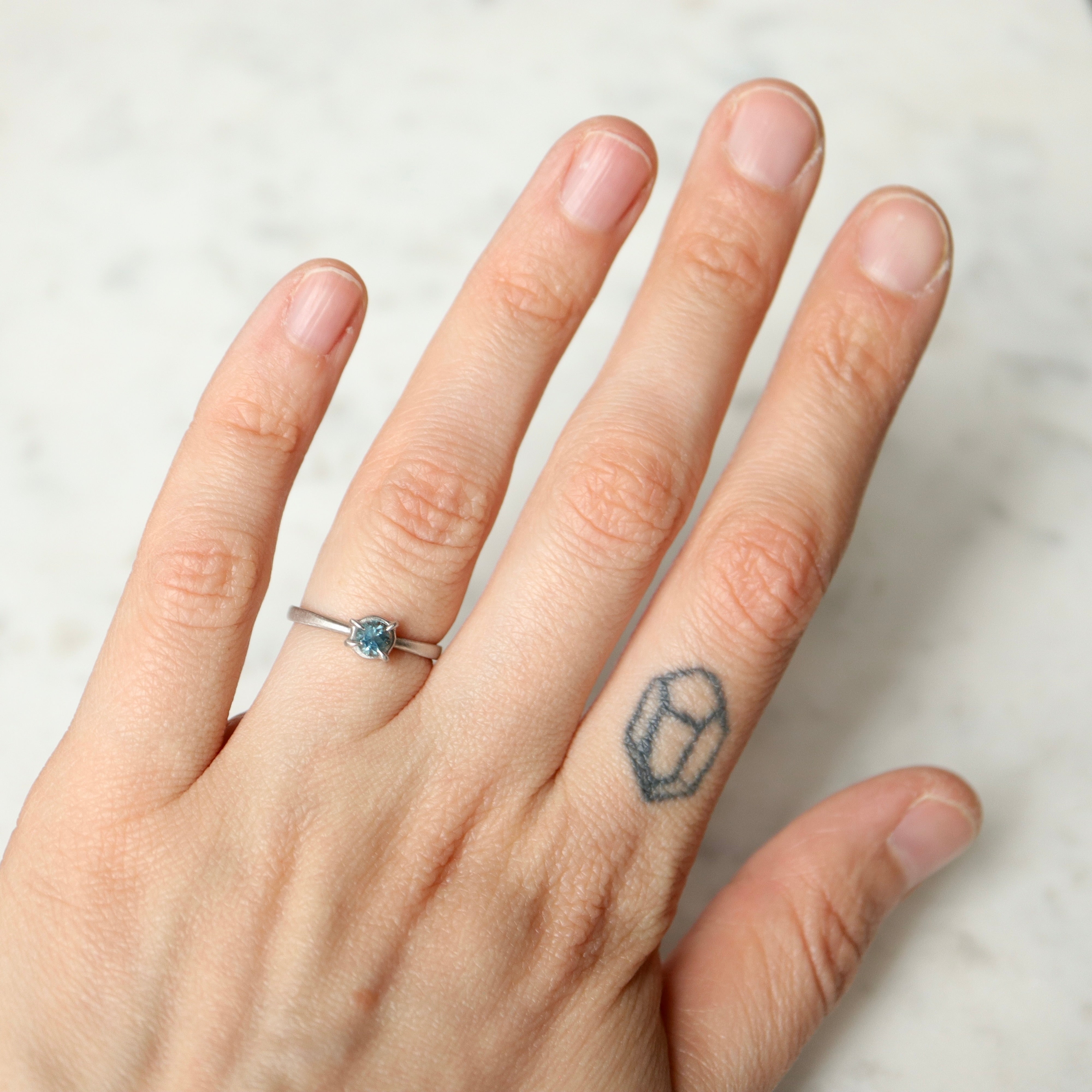 blue montana sapphire stone set in a ring of platinum via prongs- shown on hand