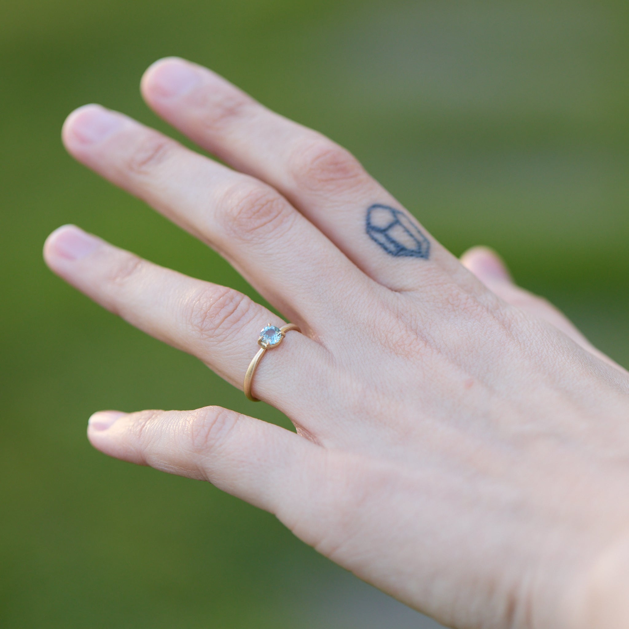 Hand with a gold ring and a small tattoo on a blurred green background